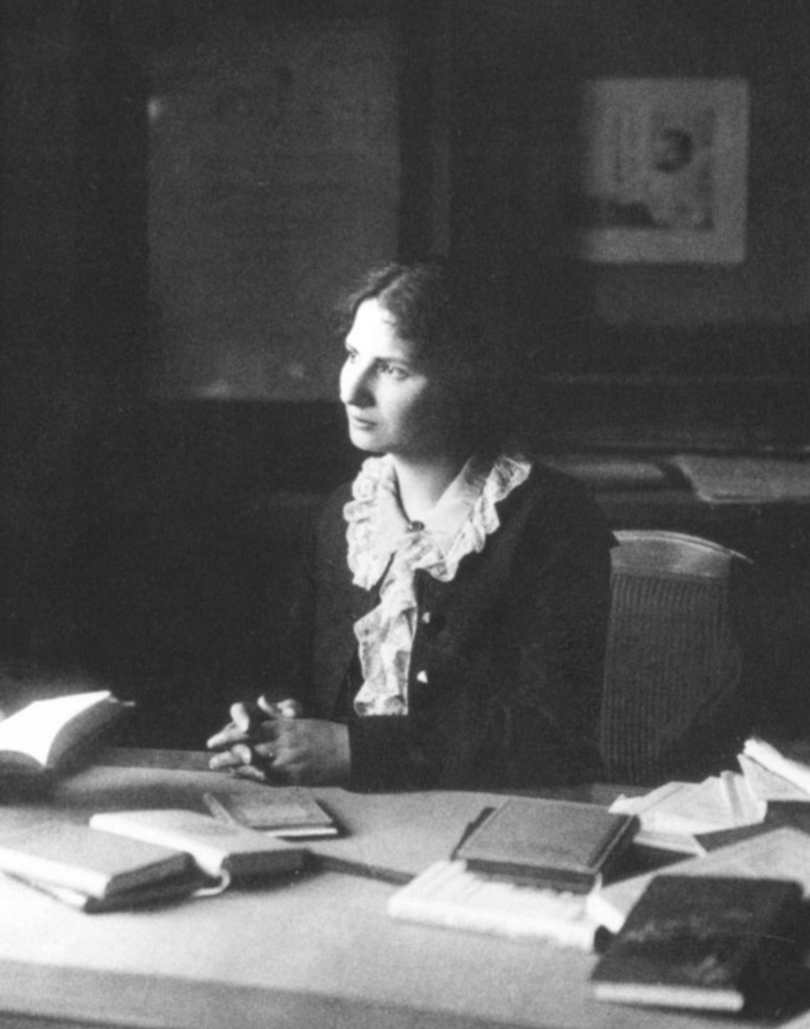 Ausschnitt der Fotografie zeigt Ida Dehmel im Nietzsche-Archiv, 1905. Sie trägt eine dunkle Jacke und einen hellen Kragen. Sie sitzt am Tisch mit Büchern. Im Hintergrund an der Wand eine Fotografie Nietzsches. Nachweis von wiki commons folgt.