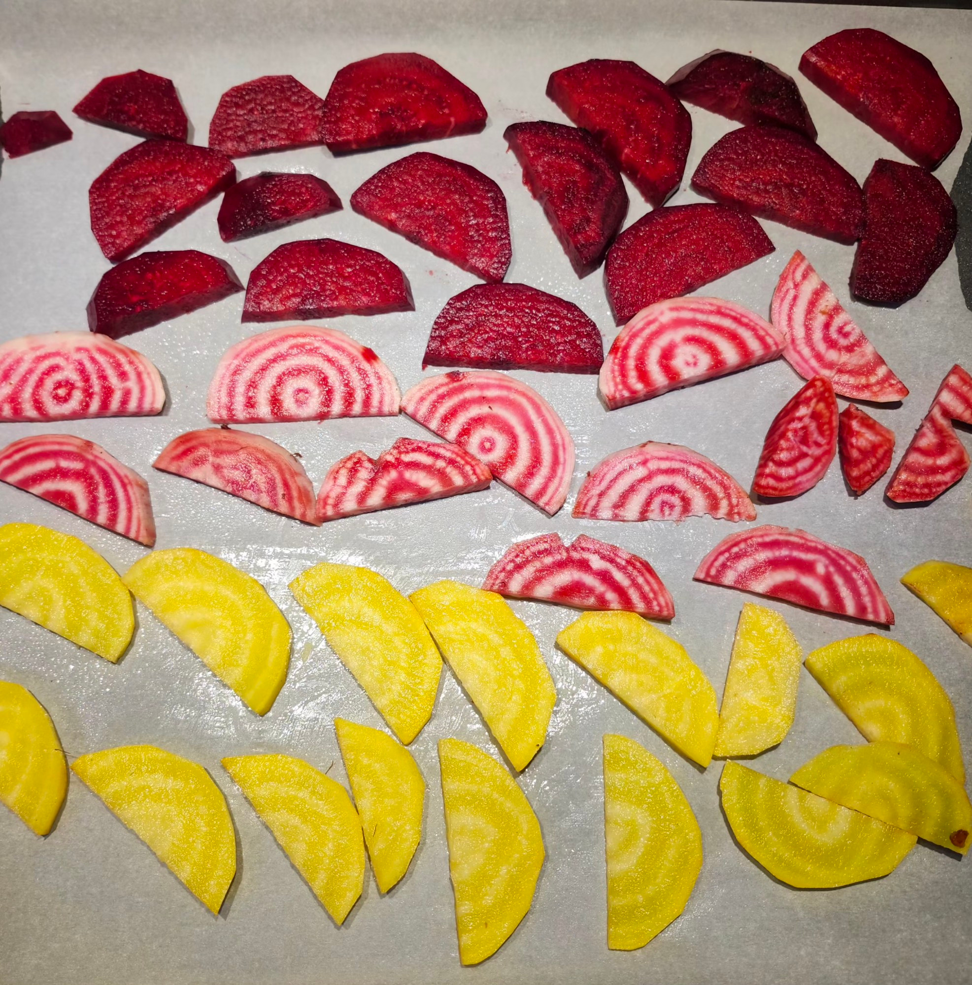 3 types of beets sliced and lined haphazardly on parchment paper. Top row: classic, deep red beets. Middle row: bullseye beets (red and white rings, hence the name) Bottom: golden beets in a bright, lemon yellow. 