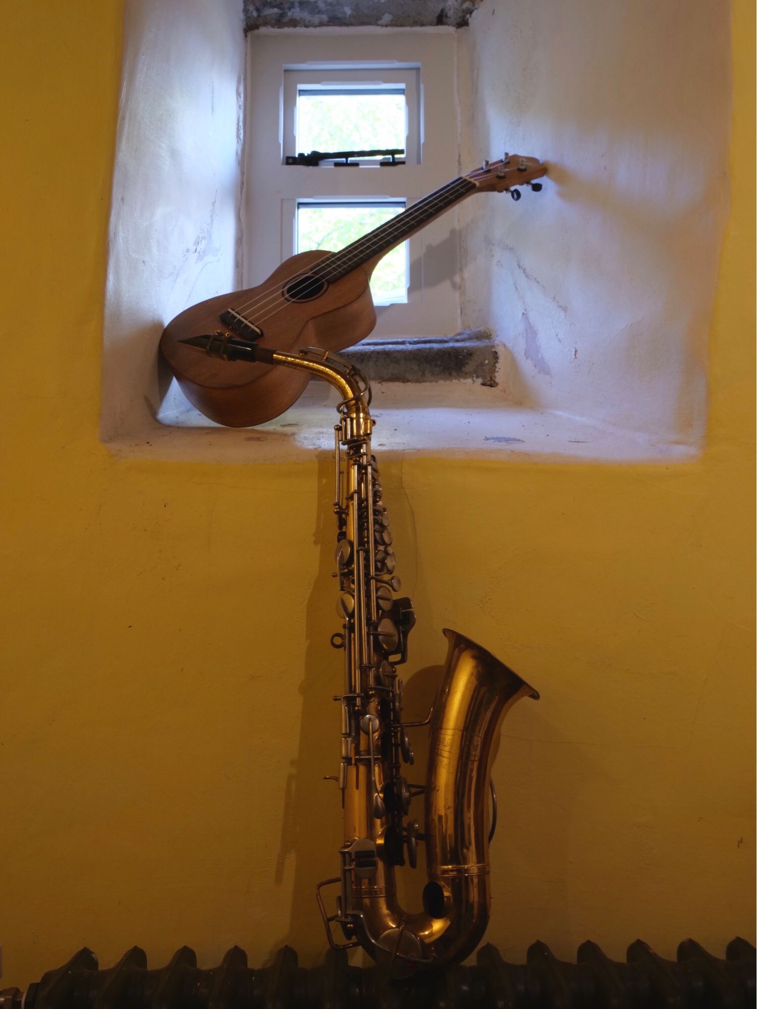 A saxophone and ukulele propped against a small window