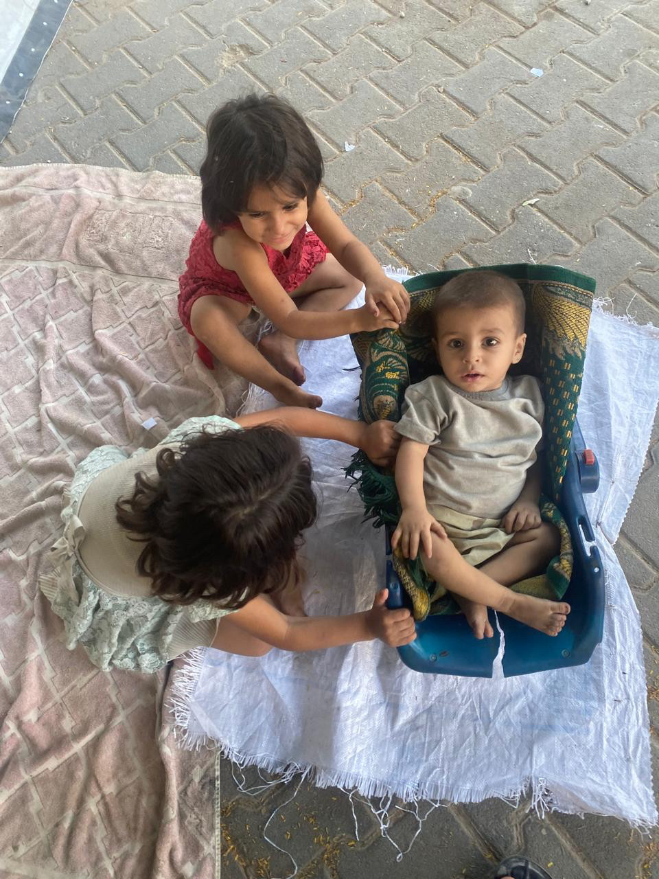 Three little kids sitting on blankets in Gaza 