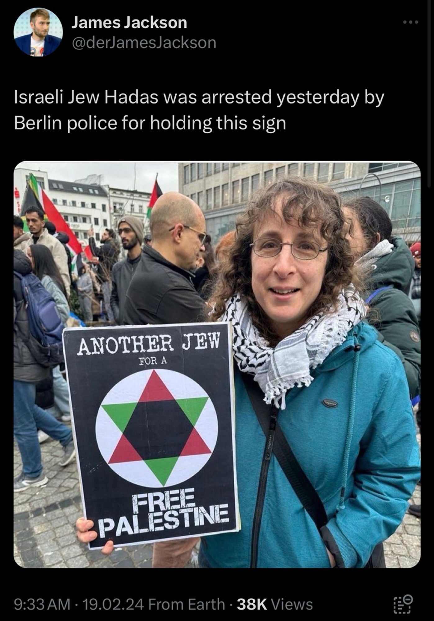 Tweet that reads: James Jackson
@derJamesJackson
Israeli Jew Hadas was arrested yesterday by Berlin police for holding this sign

Woman wearing a keffiyeh holding a sign with a Star of David in Palestinian colors that reads  

ANOTHER JEW
FOR A
FREE
PALESTINE