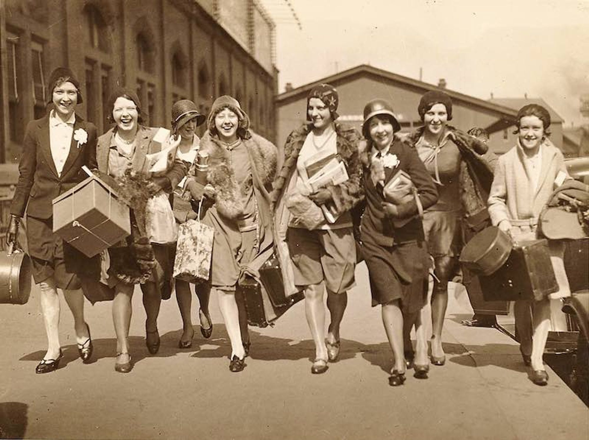 group of women in 1920s clothing walking along railroad platform carring luggage