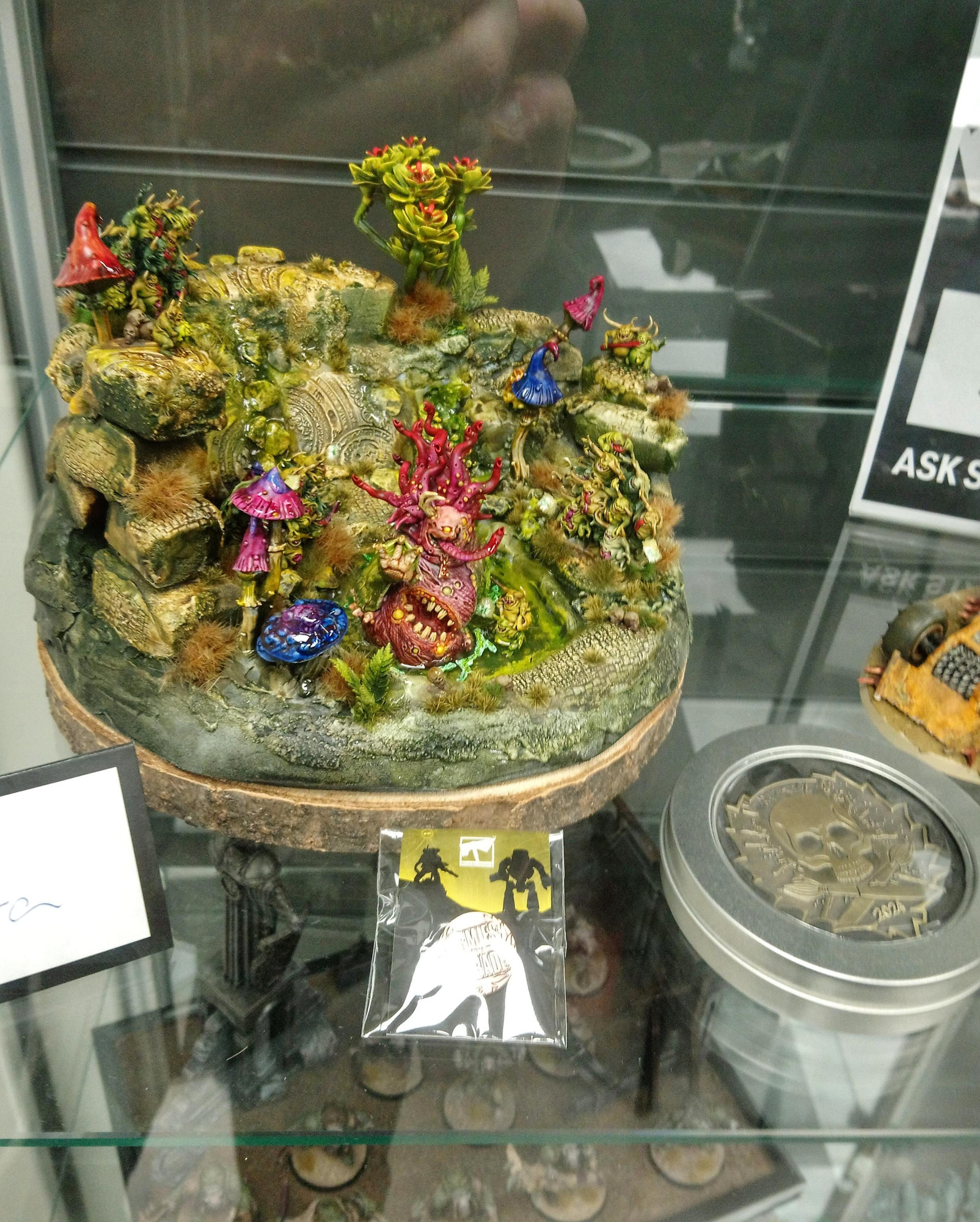 Photo of a glass showcase with a small diorama of a ruinscape with Nurglings and a bathing Beast of Nurgle in a slime pond. Next to it is a gold medal for Armies on Parade. 