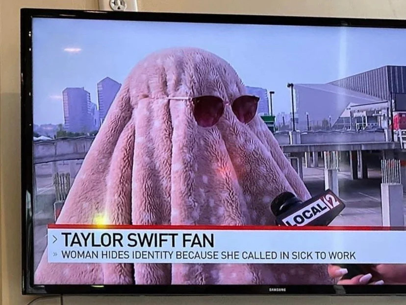 A photo of a TV where a woman dressed as a ghost for the Eras Tour is interviewed by local news. The caption reads “Woman hides identity because she called in sick to work.”