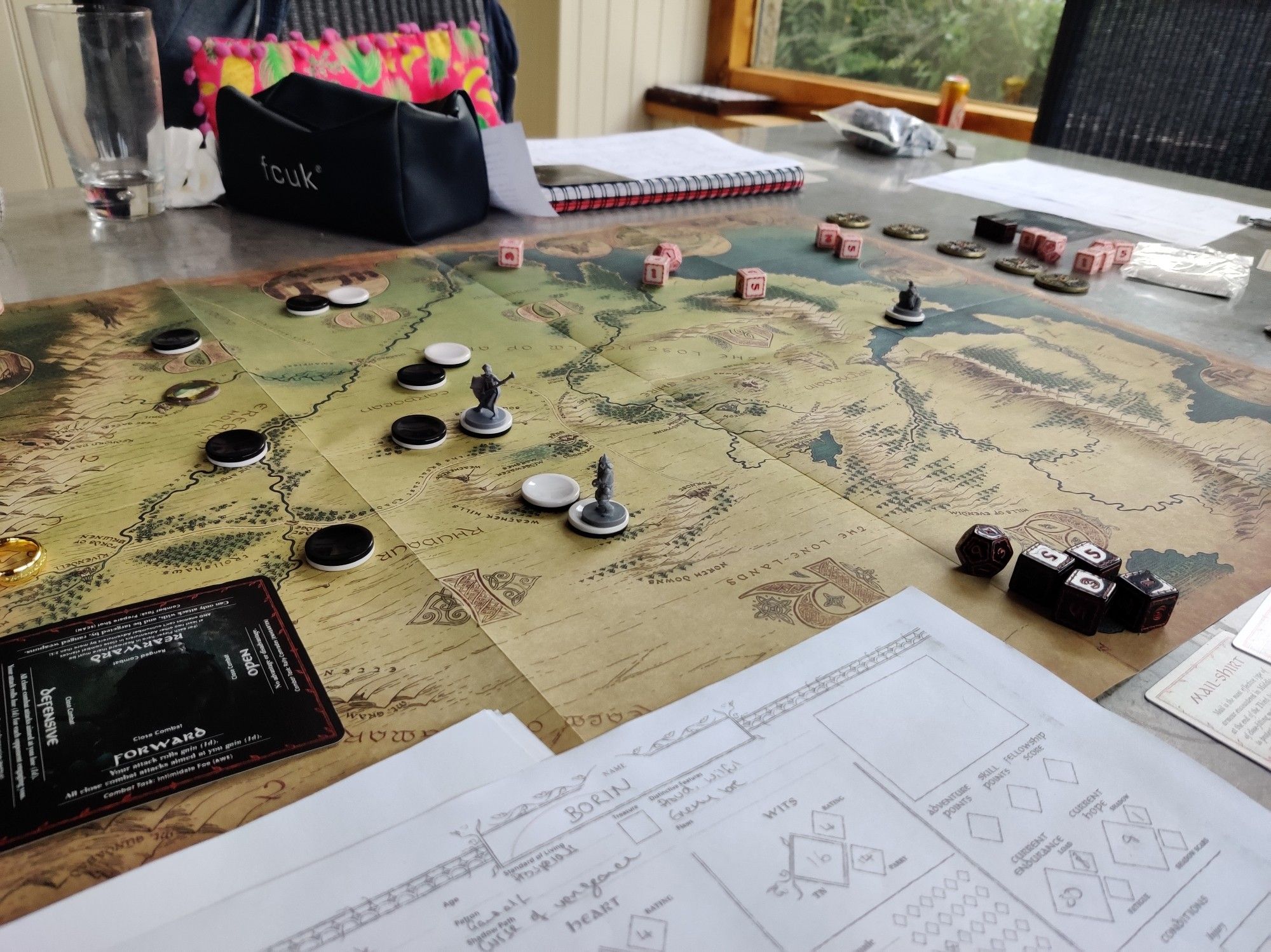 A table with a map of middle earth. Several minis, tokens, dice and character sheets litter the table