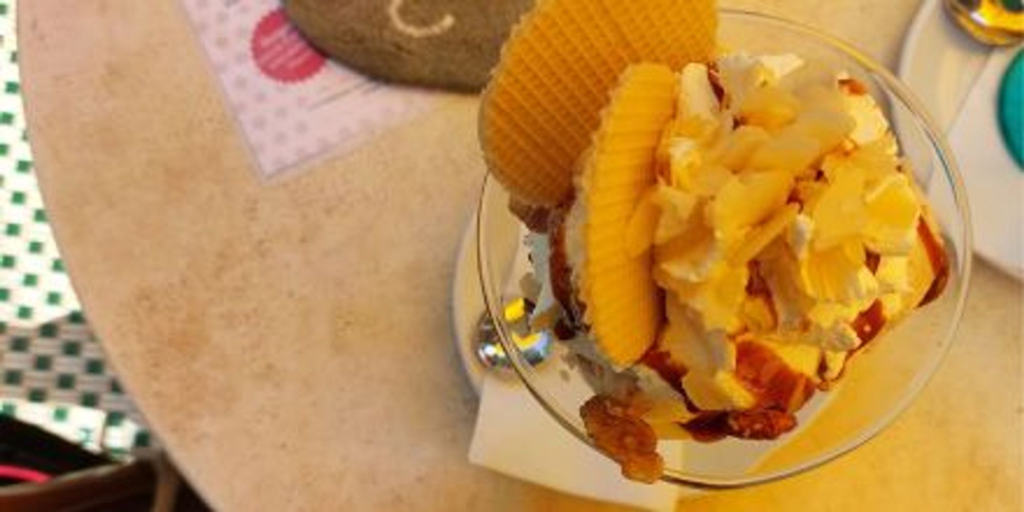 Café-Tisch, darauf ein Eisbecher mit Sahne, Waffeln und Nüssen.