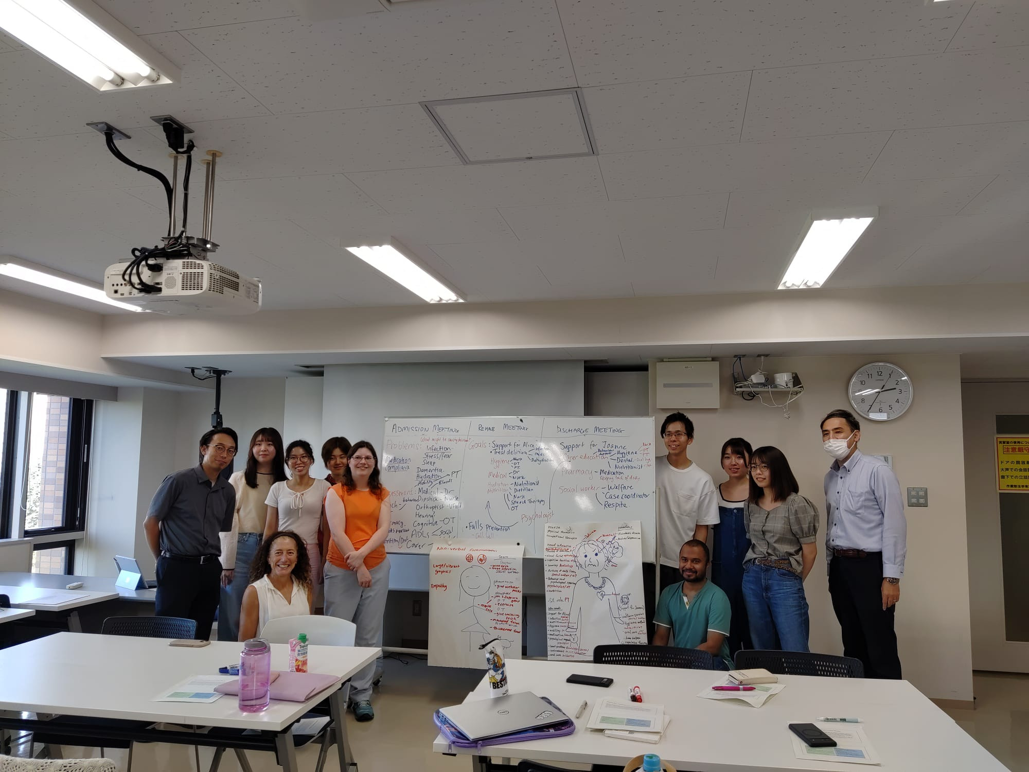 The students and teaching team standing in front of a whiteboard showing key team members and assessments reported on at each multidisciplinary team meeting during a person's admission