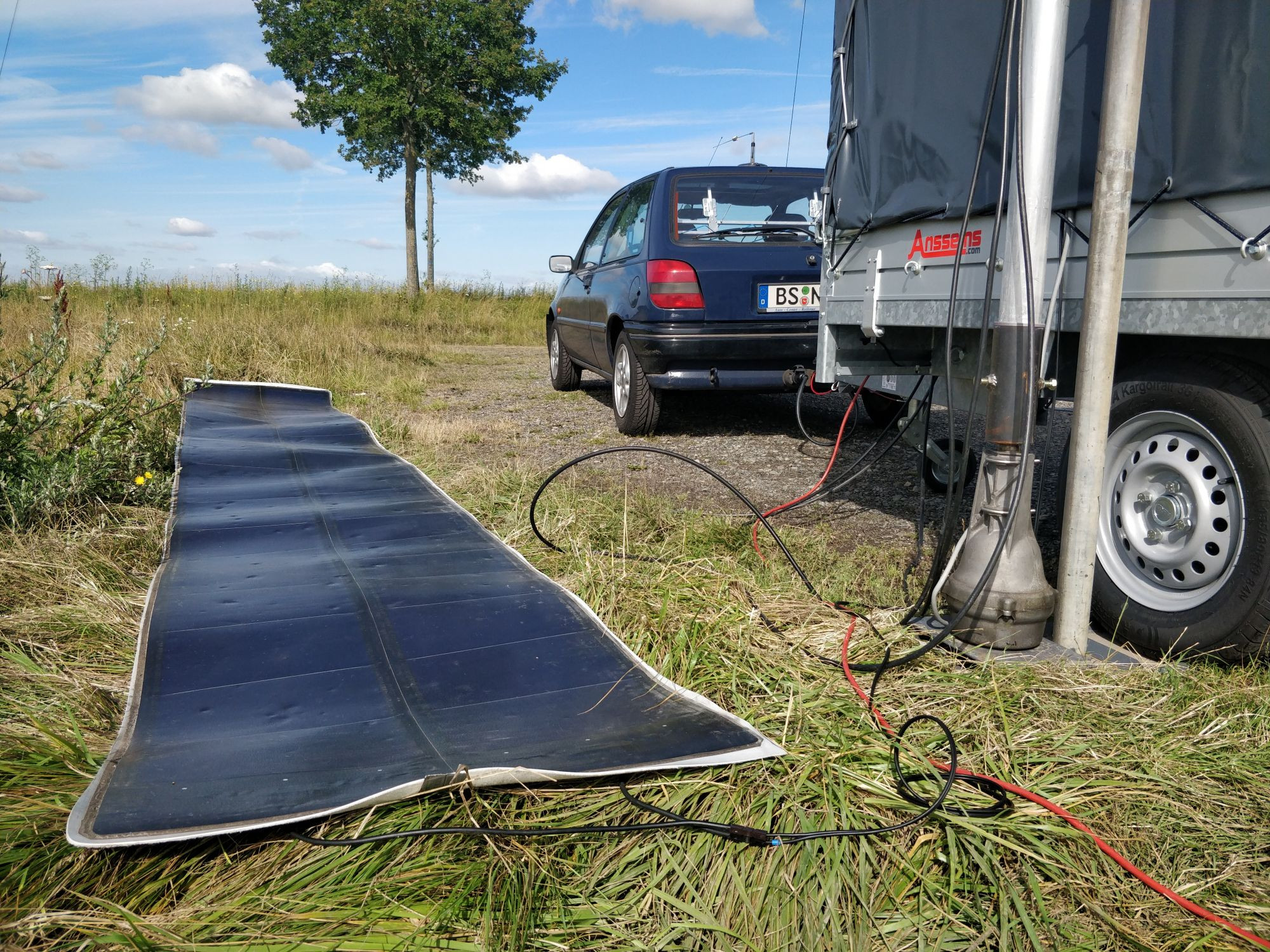 Auf dem Boden liegt eine ausgerollte Solarzelle, daneben sieht man den Auffahrfuß mit dem Rotor. Einige Kabel führen in den Anhänger