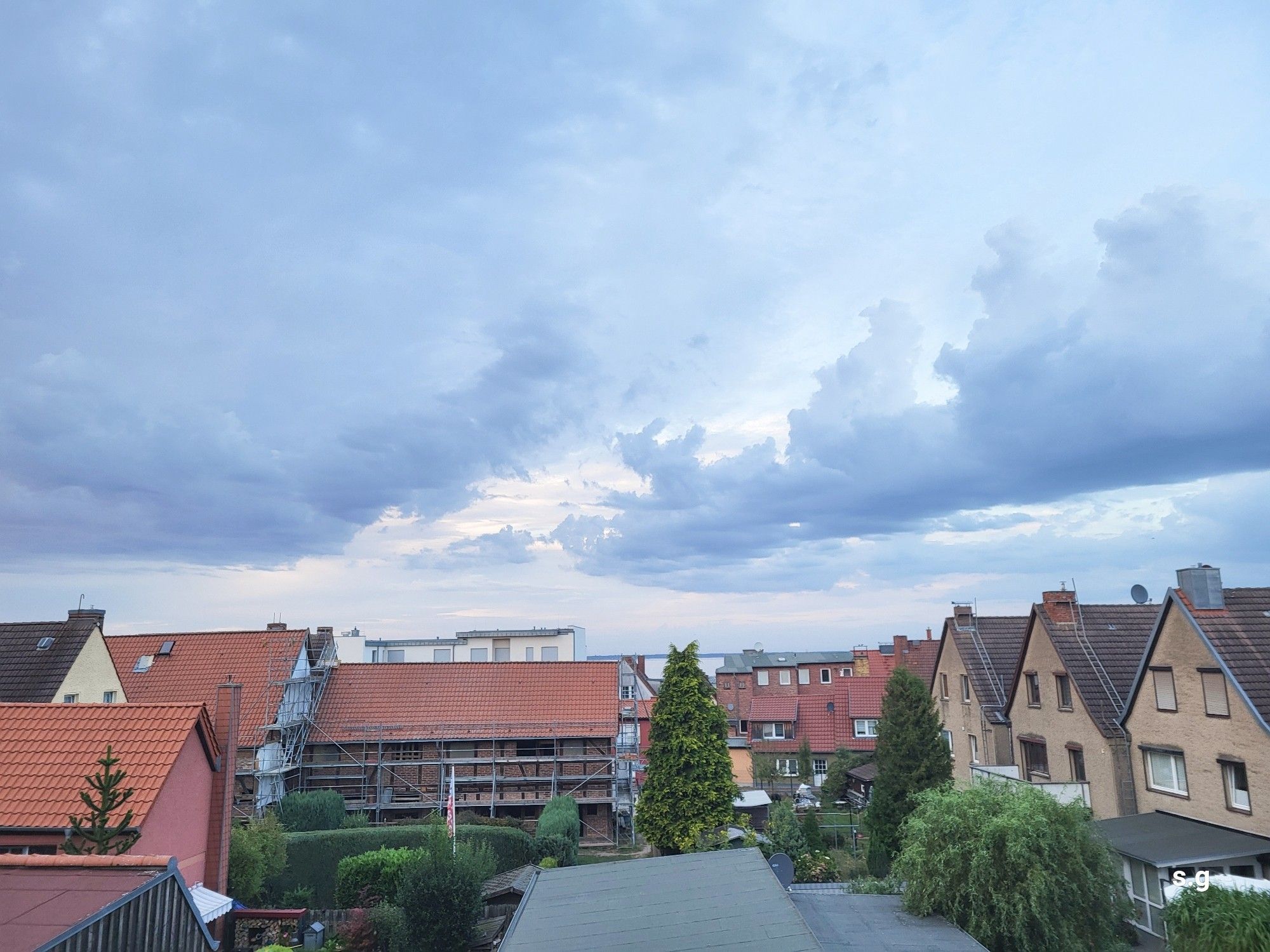 Häuser und Dächer verschiedenster Art, darüber ein Wolkenhimmel.