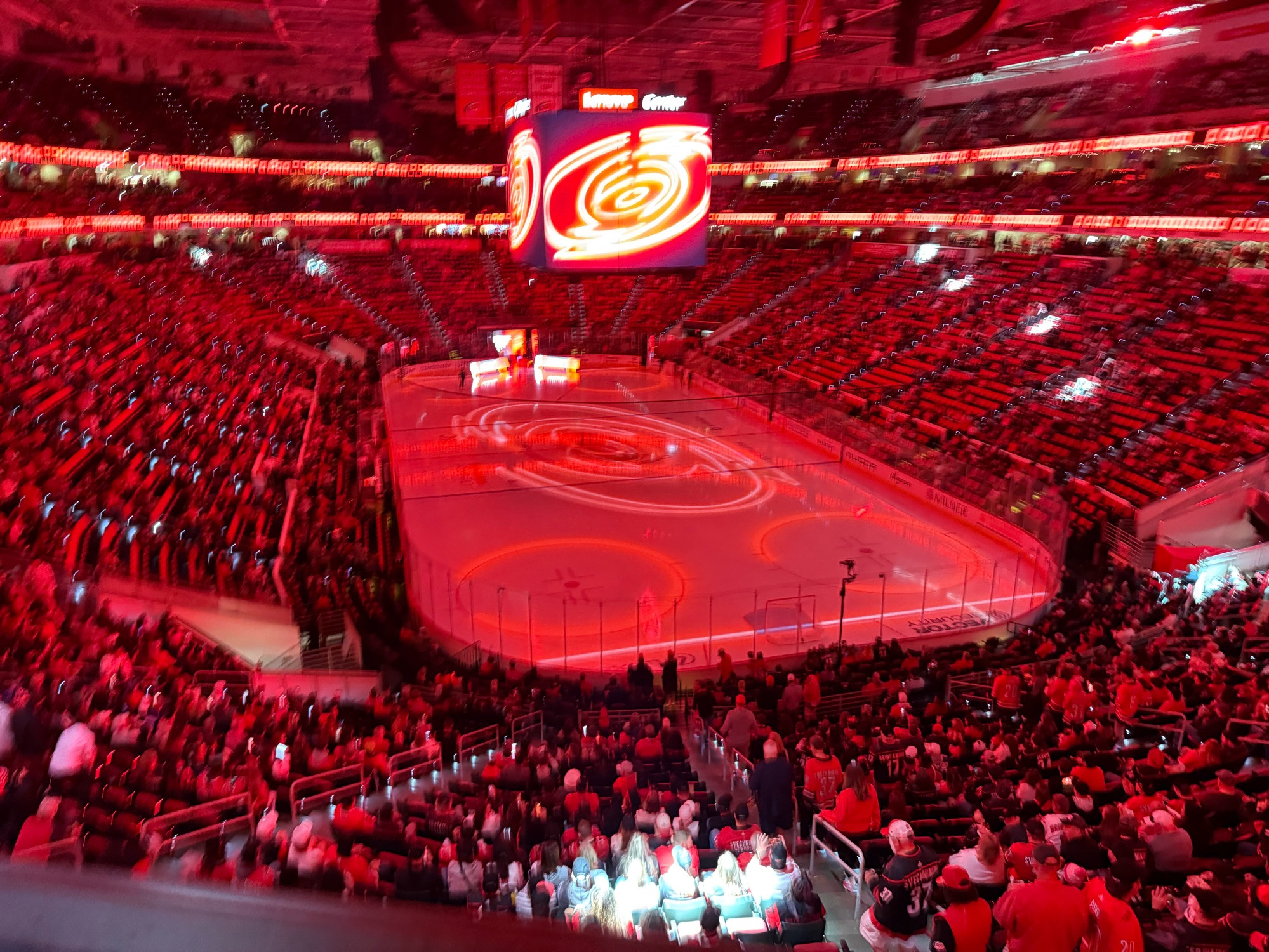 Pictured: Lenovo Center (10/11/2024), Carolina Hurricanes opening night. Displays the arena with participants covered in a red glow from lights and the hockey rink. 