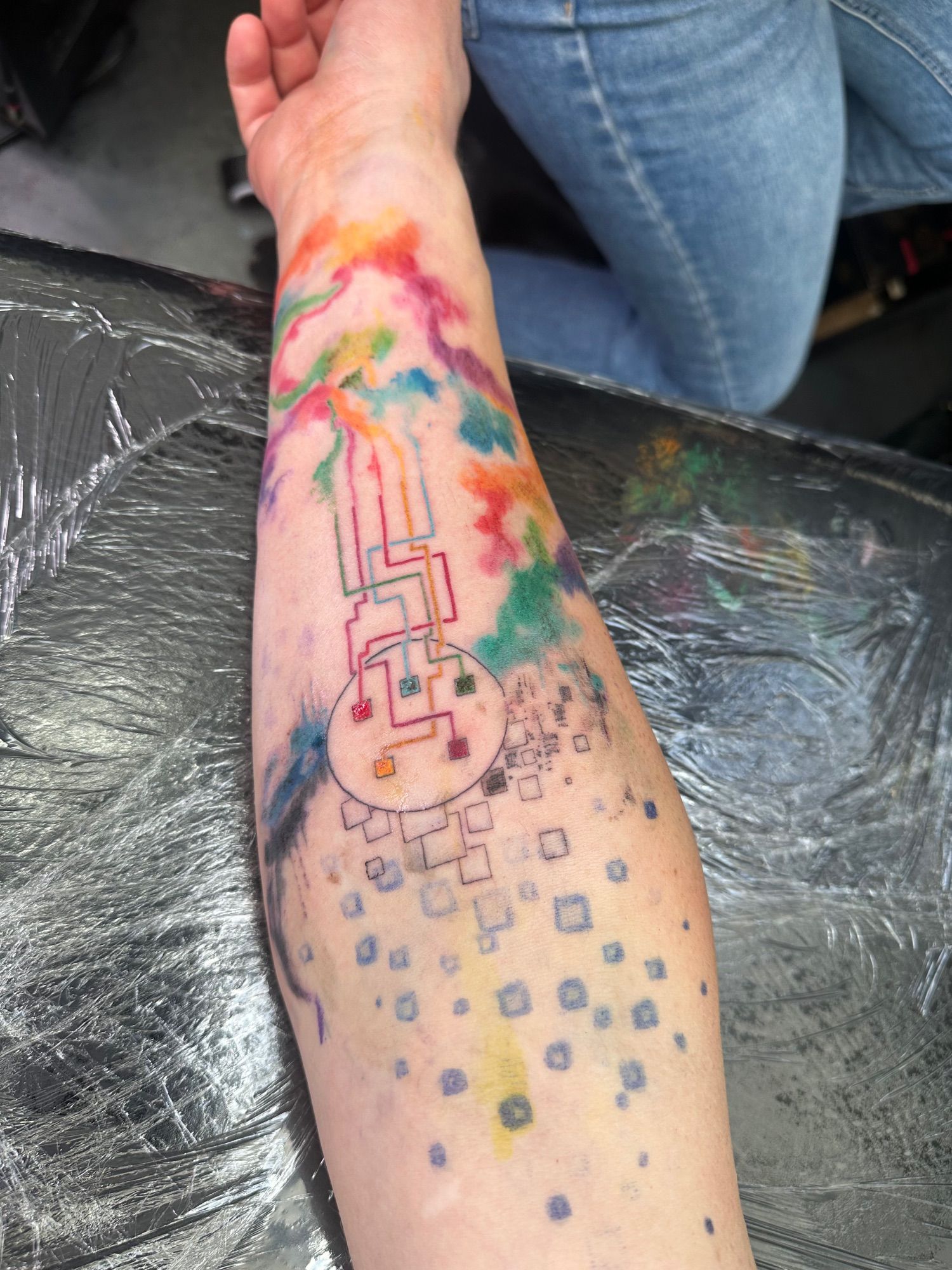 John’s forearm halfway through his tattoo session. A central circle that alludes to an XLR five cable is emanating freeform clouds of colour down to the wrist.