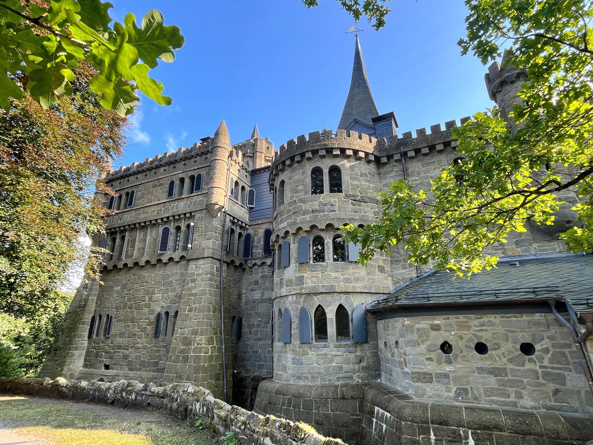 Blick auf die Löwenburg im Schlosspark Wilhelmshöhe 

Im Vordergrund ein grüner Zweig von rechts und der Teil eines Baumes zur linken.