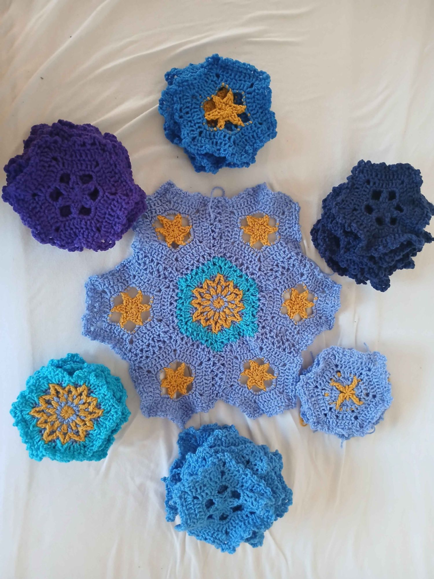 photo of several blue and purple hexagons with yellow star motifs, spread out on a white blanket