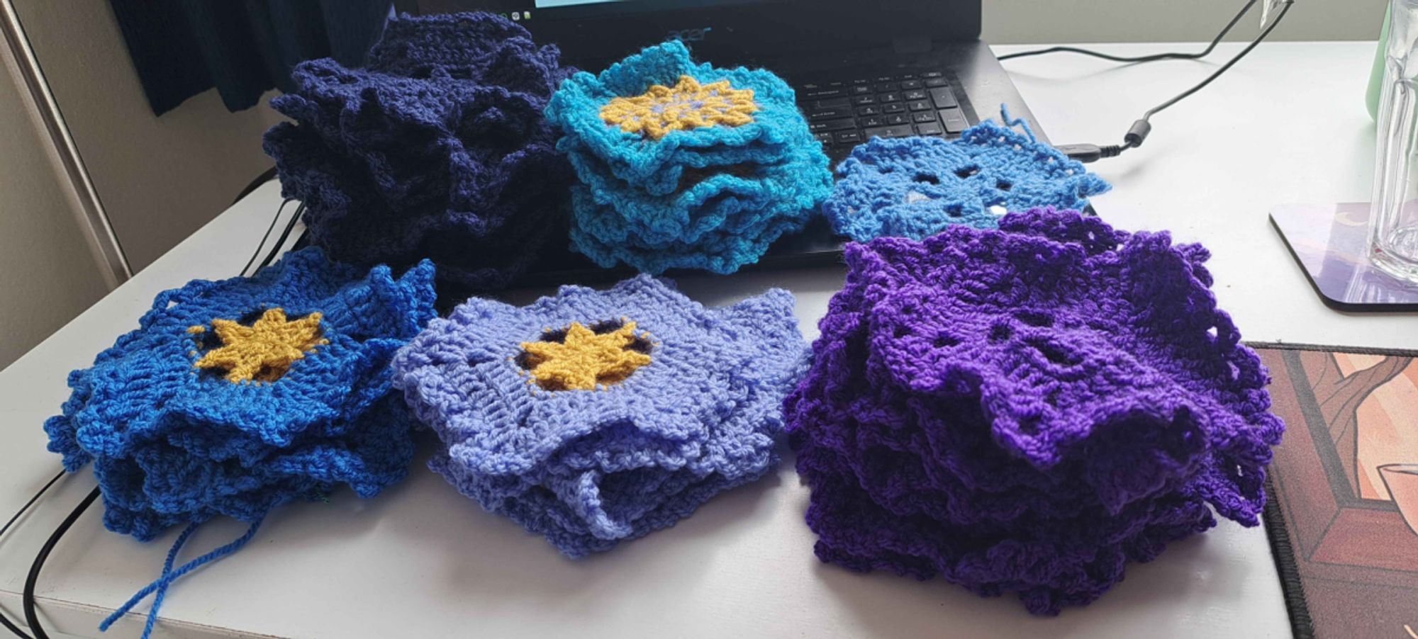 photo of six stacks of crocheted hexagons in various colors of blue, cyan, and purple. Some of the hexagons have yellow stars in their patterning.