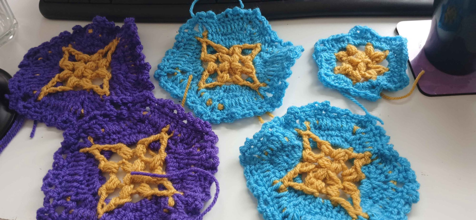 photo of four completed hexagons and one not-yet-finished hexagon, three blue ones and two purple ones, each with a yellow star at the center.