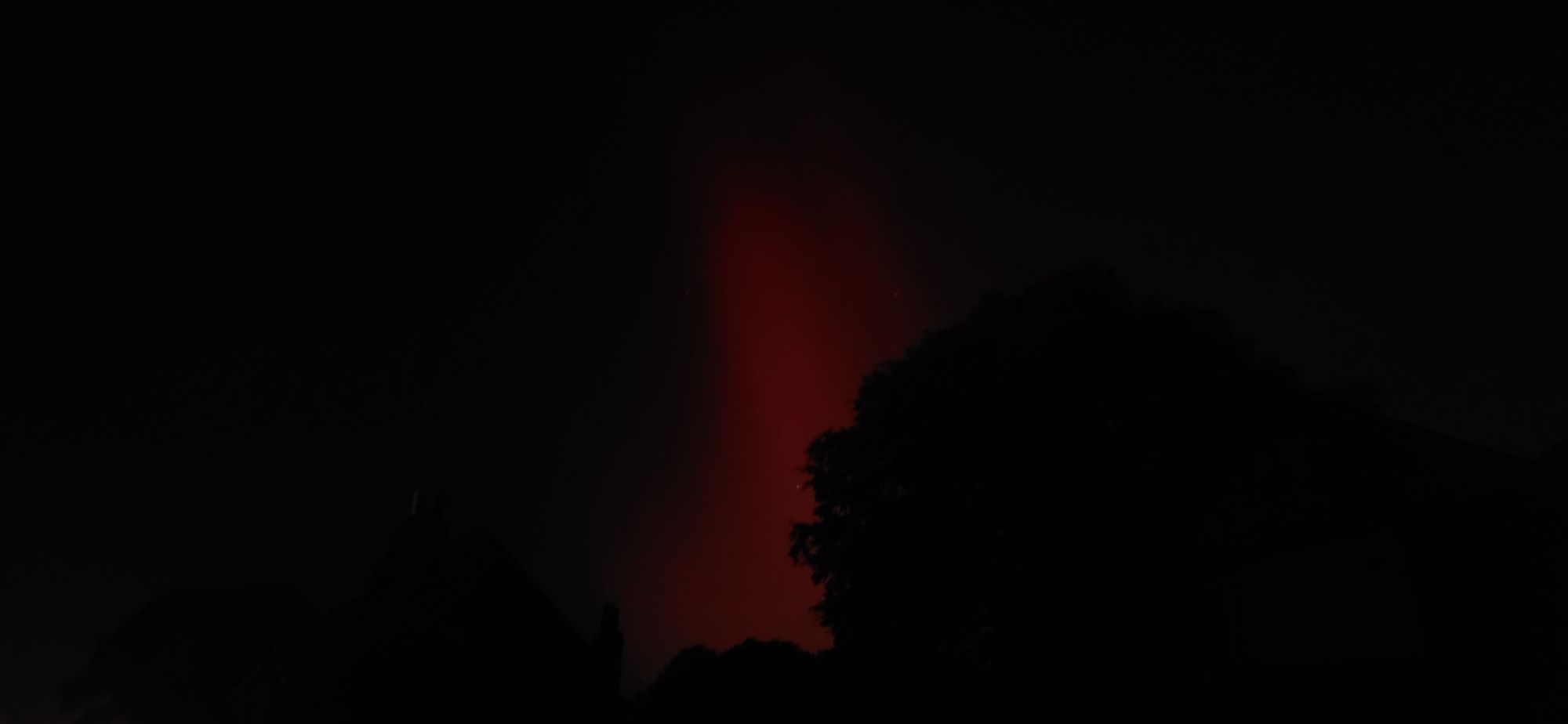 Red streak of northern lights against black sky.