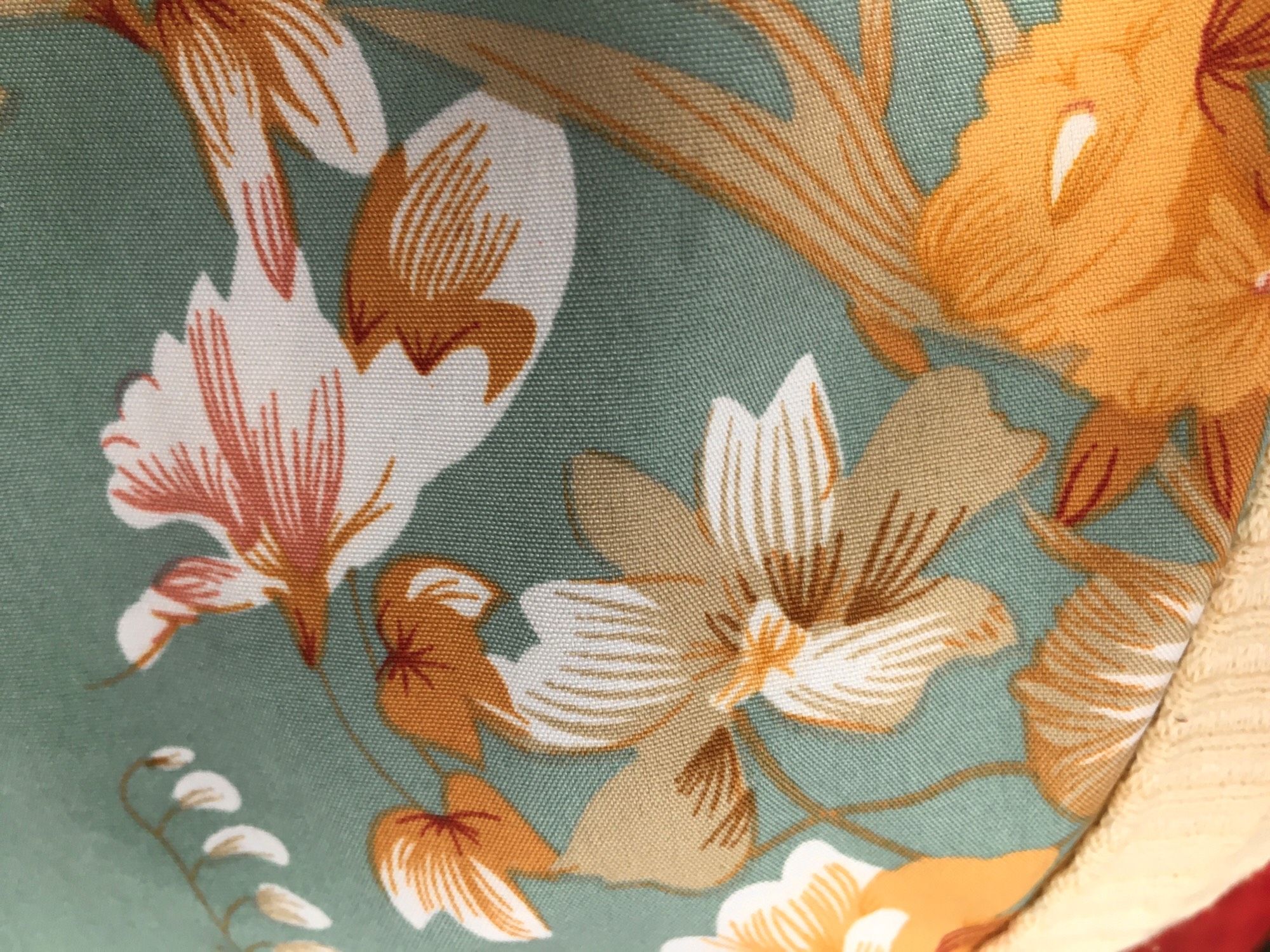 Close up of a floral print with sage green background and flowers and leaves in a range of colours from taupe to mustard to rust red.