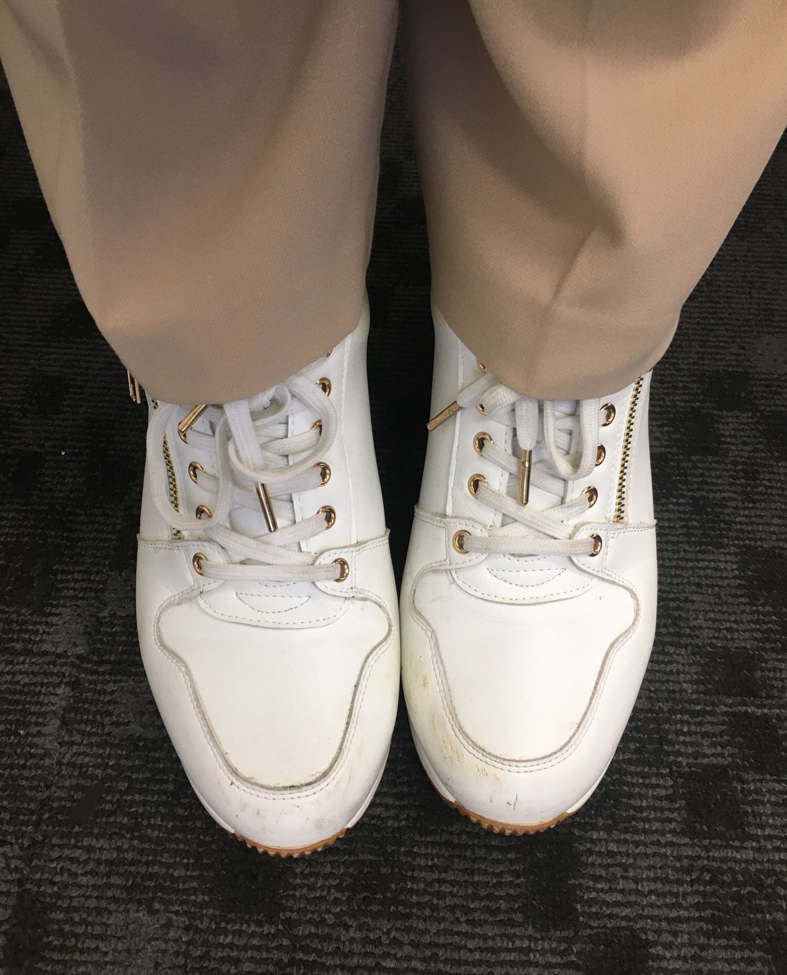 White sneakers peeking out from tan wide legged trousers.