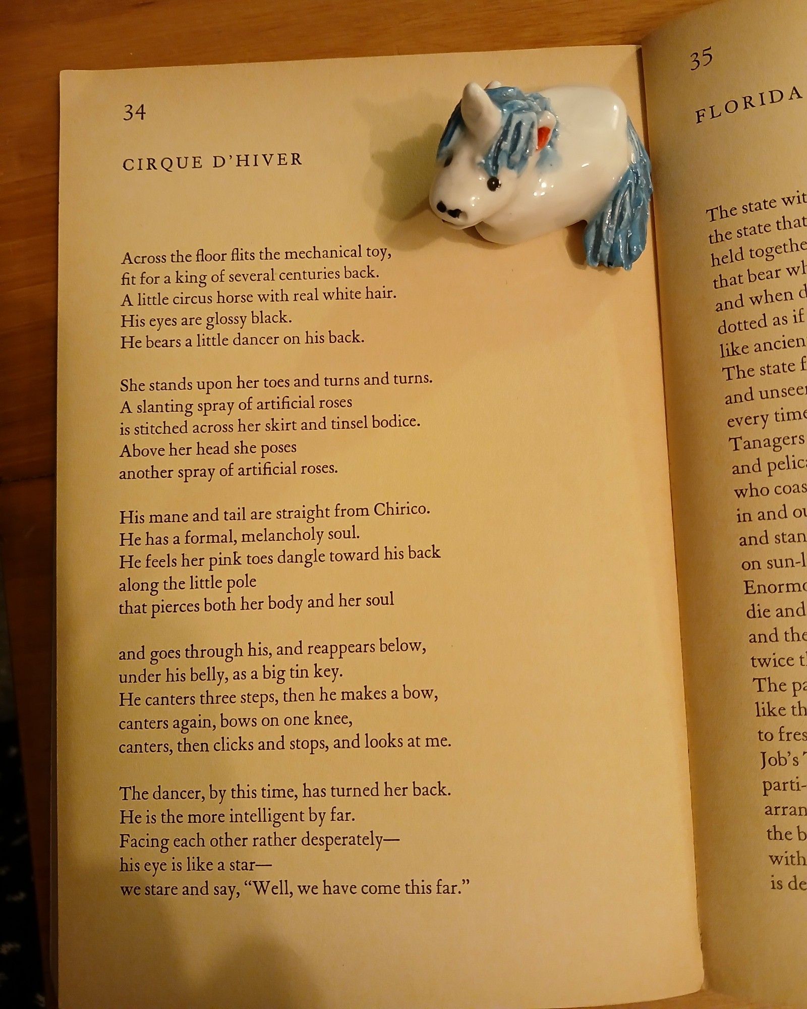 Image of 'Cirque d'Hiver' by Elizabeth Bishop: the page is pinned down by a small ceramic figurine of a unicorn.