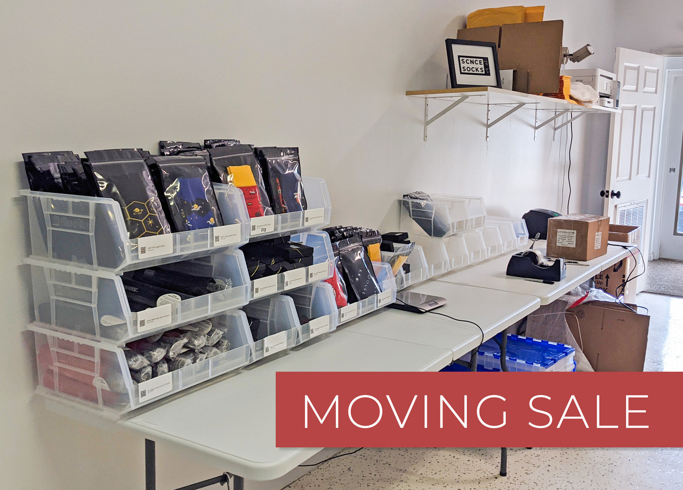 Behind the scenes photo of new ScienceSocks studio displaying racks with products like socks, umbrellas, jewelry. Text overlay: moving sale