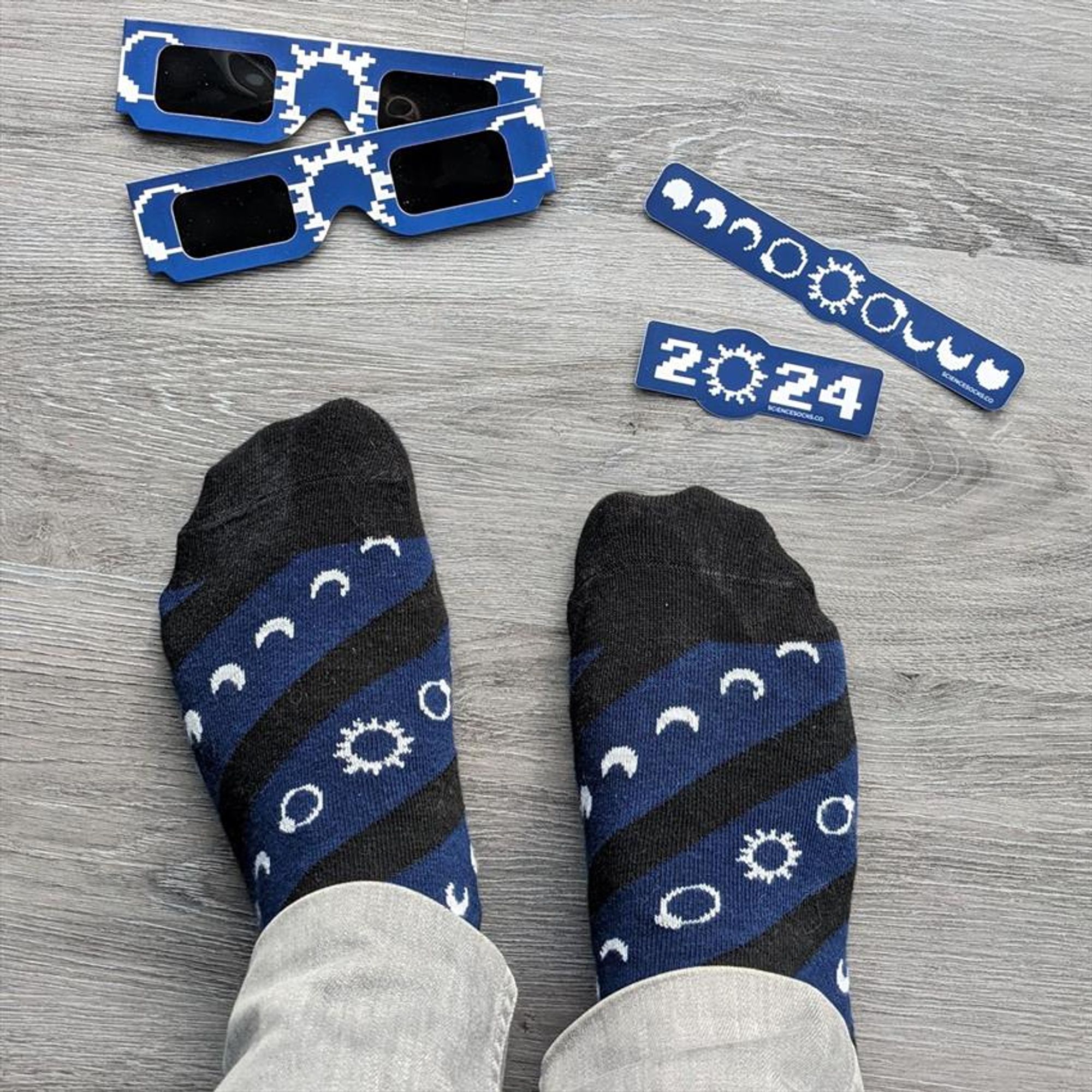 Daniel. wearing blue eclipse socks. Matching eclipse glasses and stickers laying on the floor.