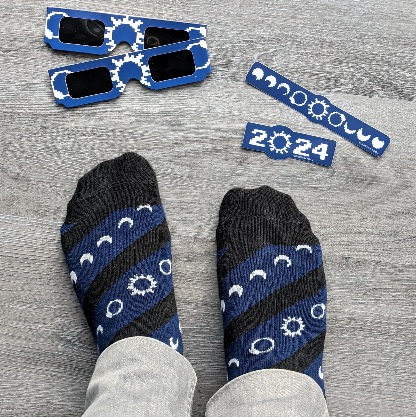 Blue solar eclipse glasses, socks and stickers featuting retro 8-bit artwork of the total eclipse sequence in white.