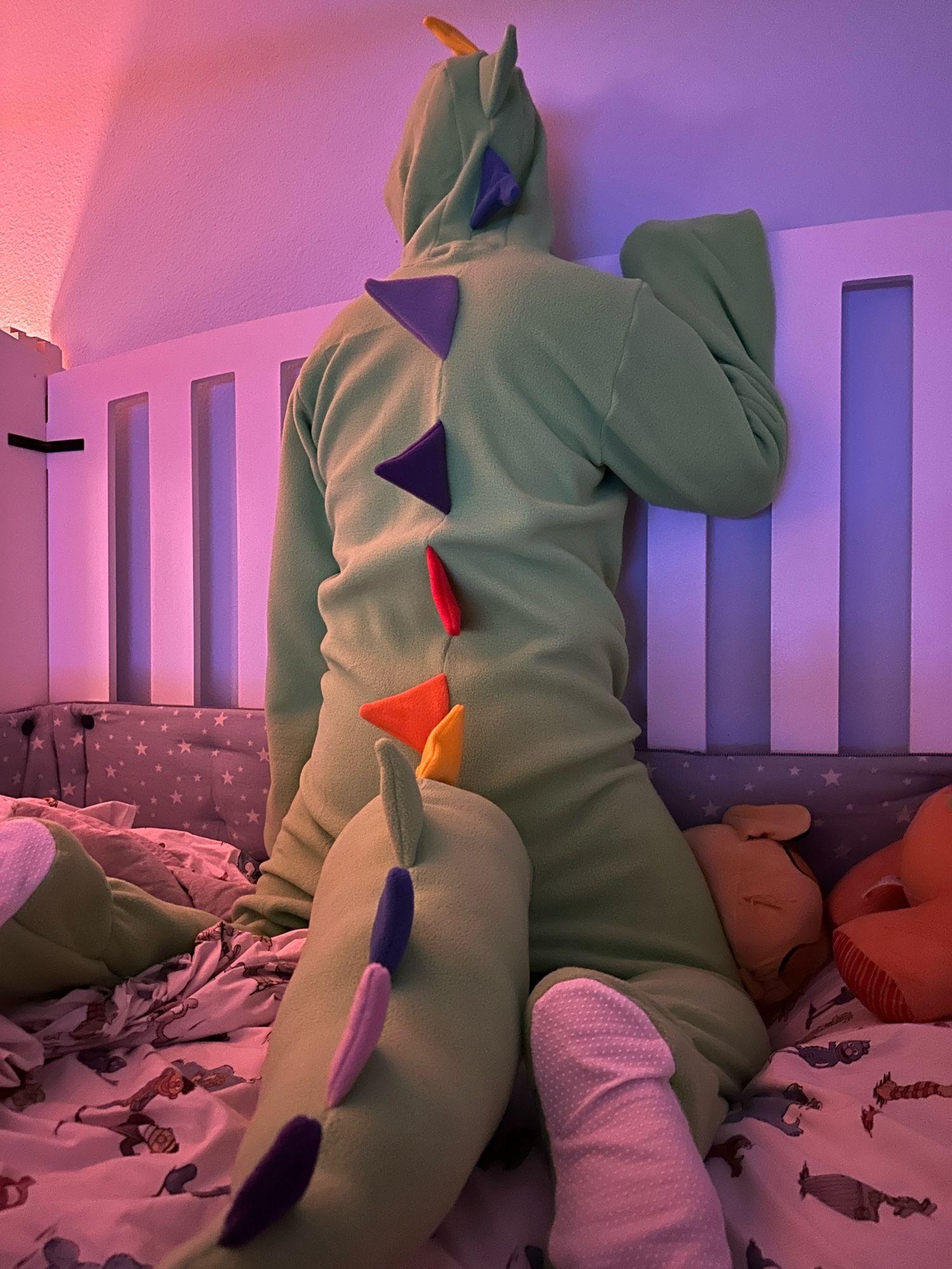 A smol puppy in dinosaur footy pajamas, getting settled in his crib.