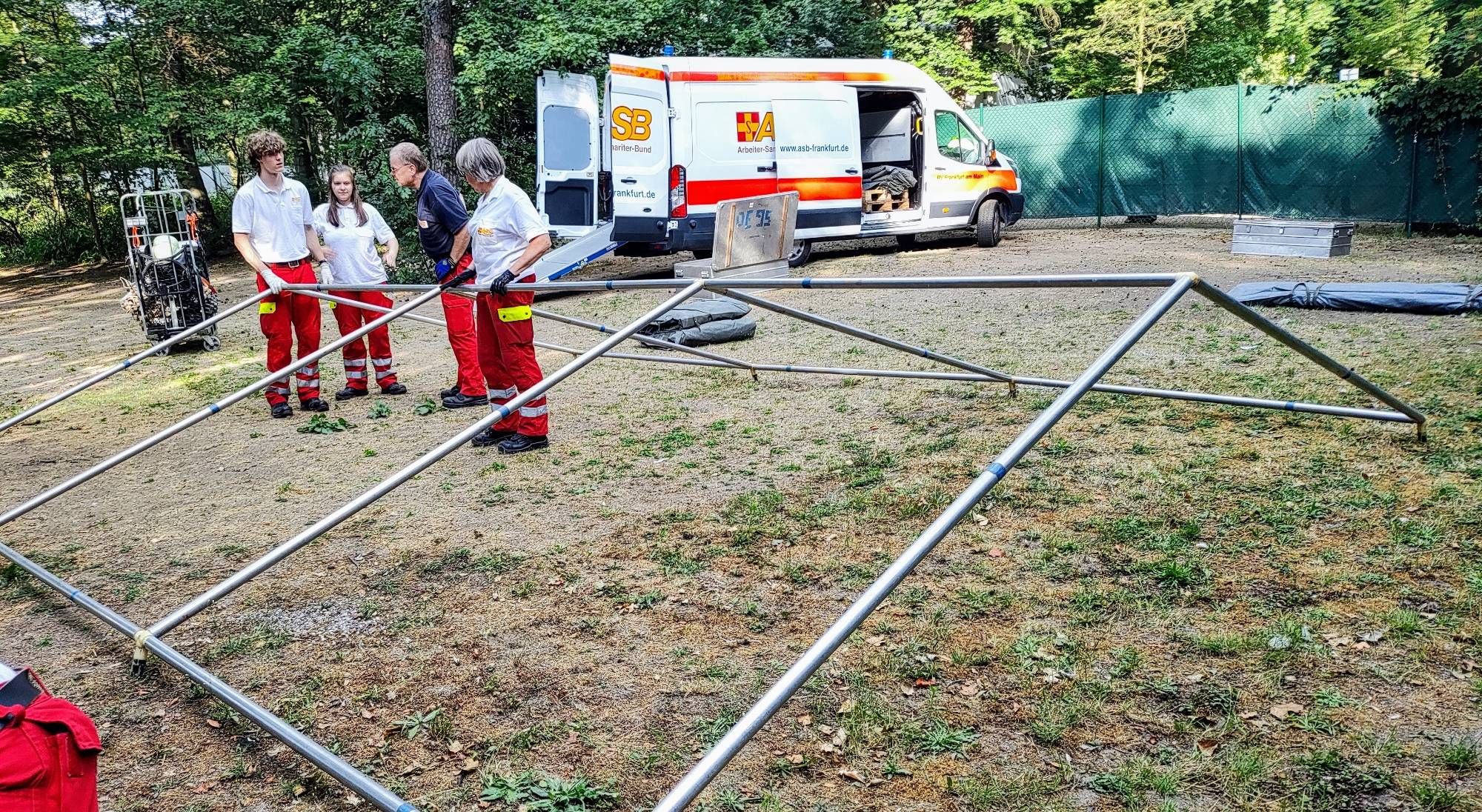 Vier Personen bauen ein Zelt auf. Im Hintergrund ein Transporter vom ASB