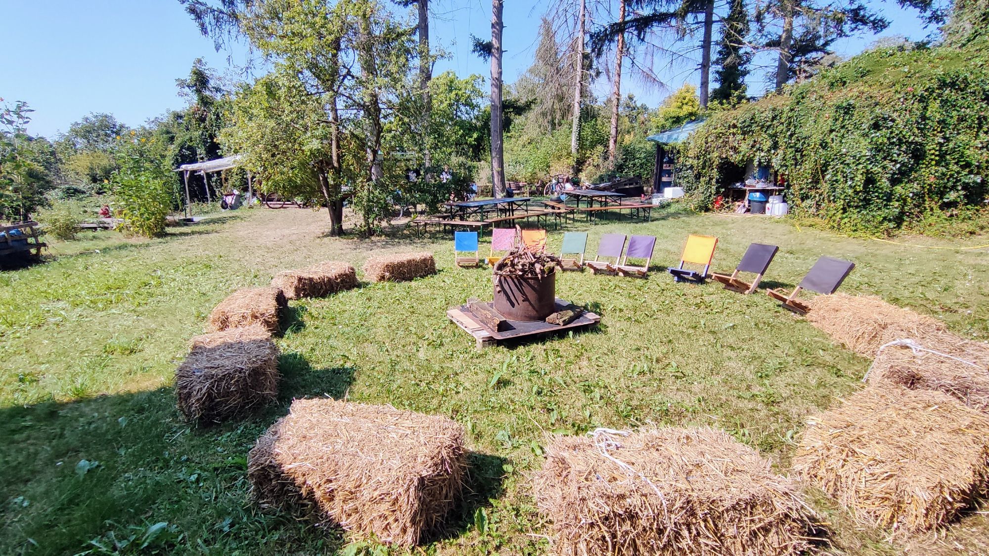 Feuerschale auf Wiese, darum Klappstühle und Strohballen, Im Hintergrund Festzeltgarnituren und Bäume