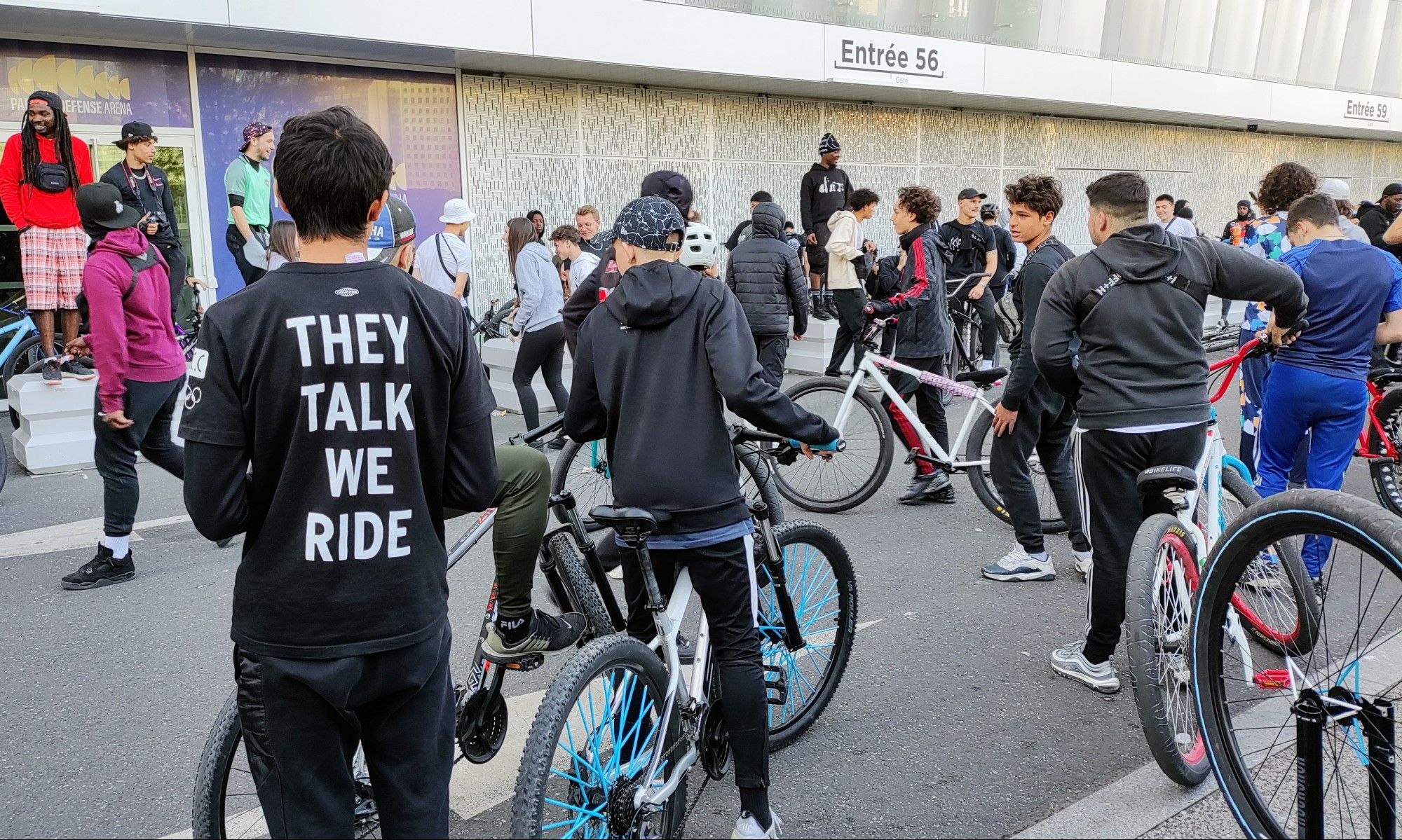 Junge Leute mit Fahrrädern. Einer trägt ein schwarzes shirt mit der Aufschrift "They talk, we ride"