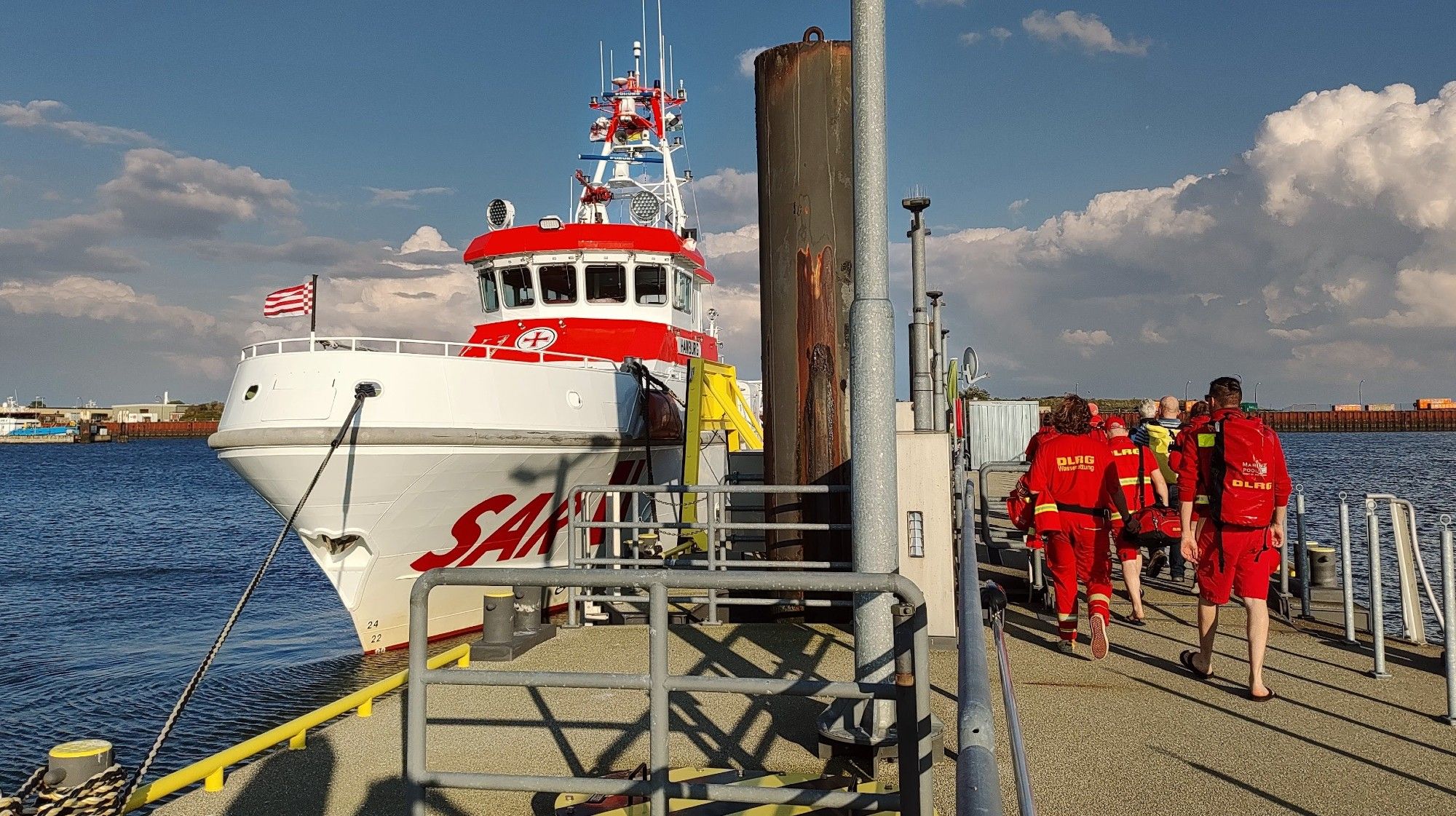 Seenot Rettungsschiff am Anleger. Rechts im Bild gehen Personen in roten DLRG Klamotten auf das Boot zu.