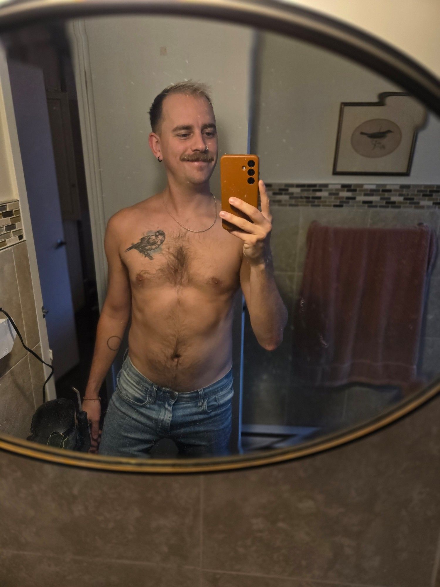 I'm standing shirtless wearing blue jeans in front of my bathroom mirror, taking a selfie.