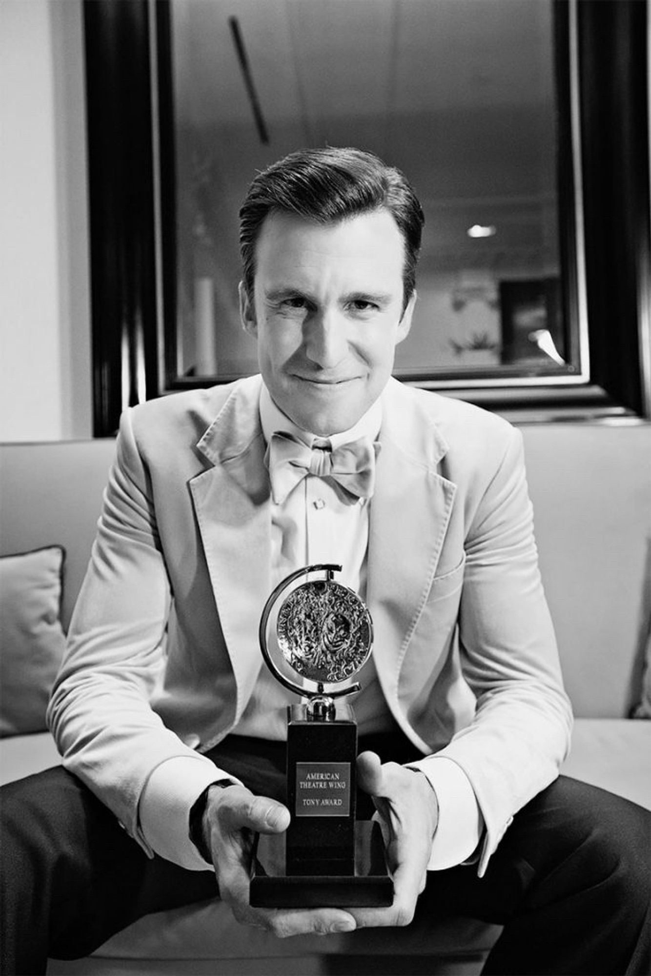 BW photo of Gavin Creel, clad in a tuxedo, smiling and holding his Tony Award