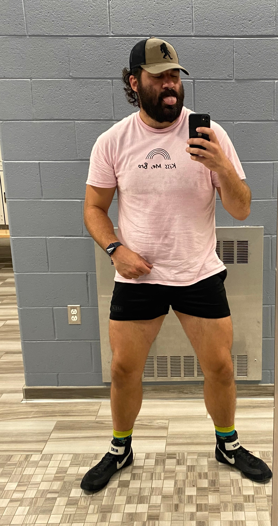 Hogie in the gym locker room fully clothed. Pink shirt that says “kiss me bro” but backwards bc it’s a mirror pic. 