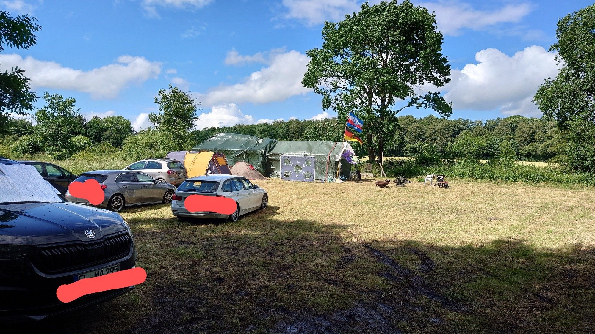 Wiese mit Autos und Zelten, darüber blauer Himmel