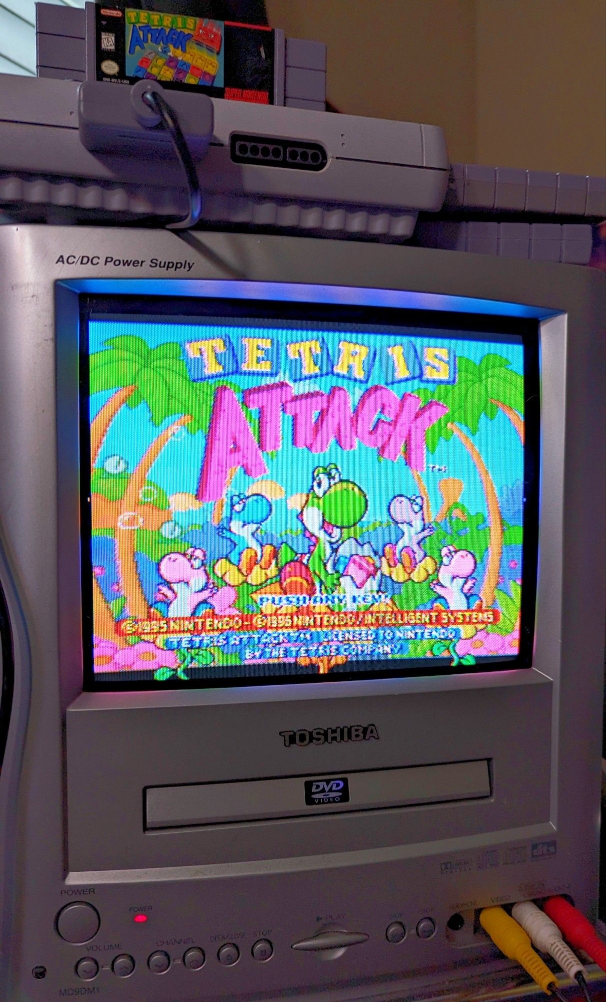 A small 9 inch CRT television displaying the title screen for Tetris Attack, which is a Super Nintendo game.