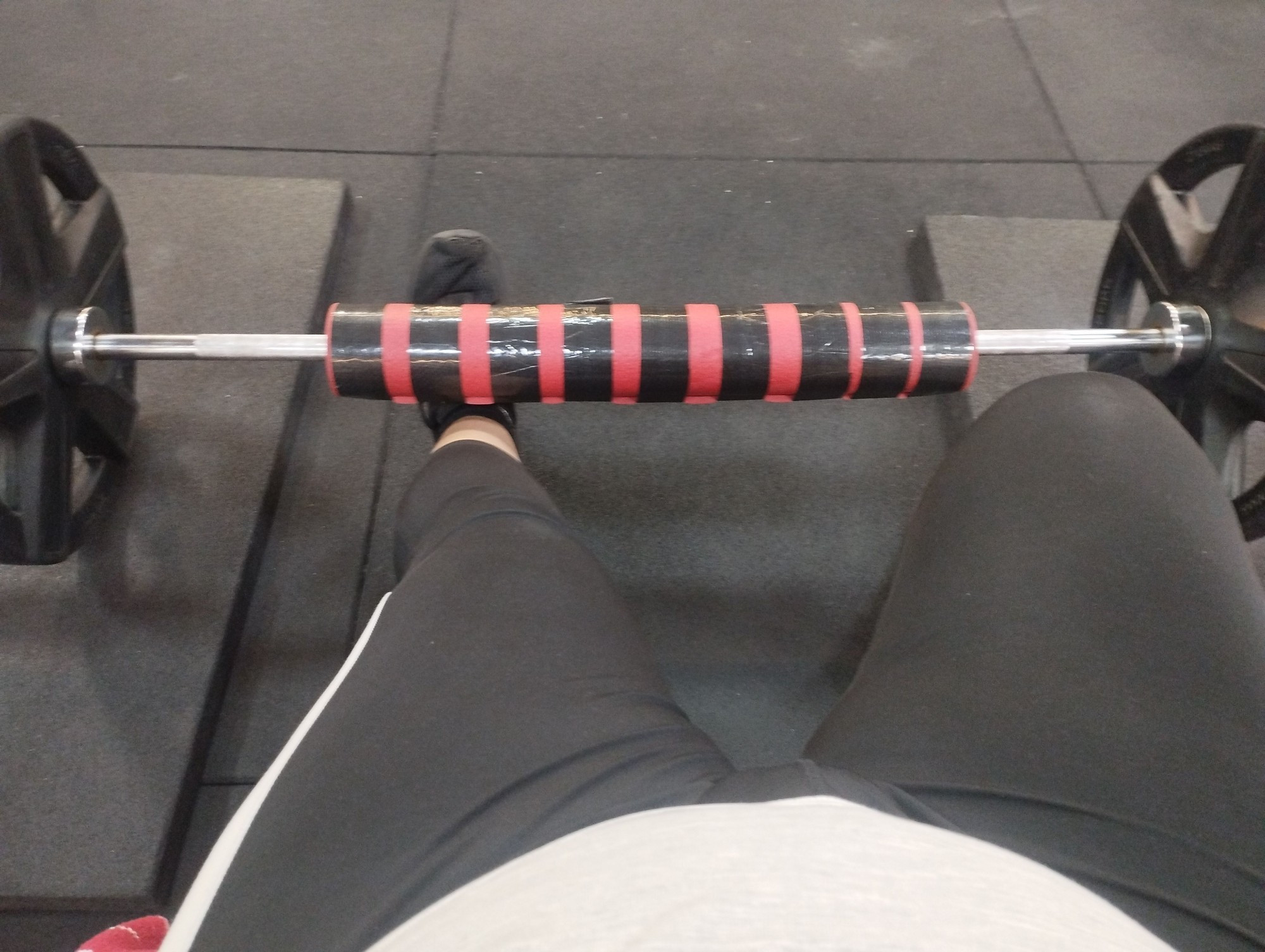 Foto de la barra cargada con 20 kilos por lado para hacer hip thrust. También se ven mis piernas con leggins negros