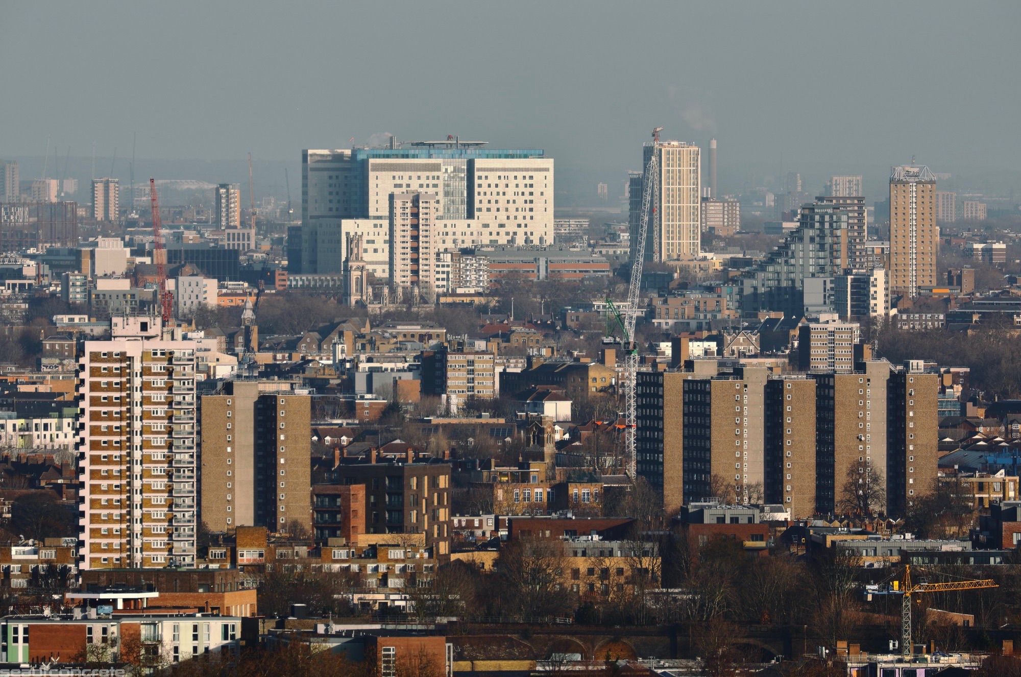 The Royal London Hospital is illuminated by morning February sunshine on a clear day, seen from Dawson’s Heights. In the foreground, the brown tower blocks of the Ledbury Estate are visible.