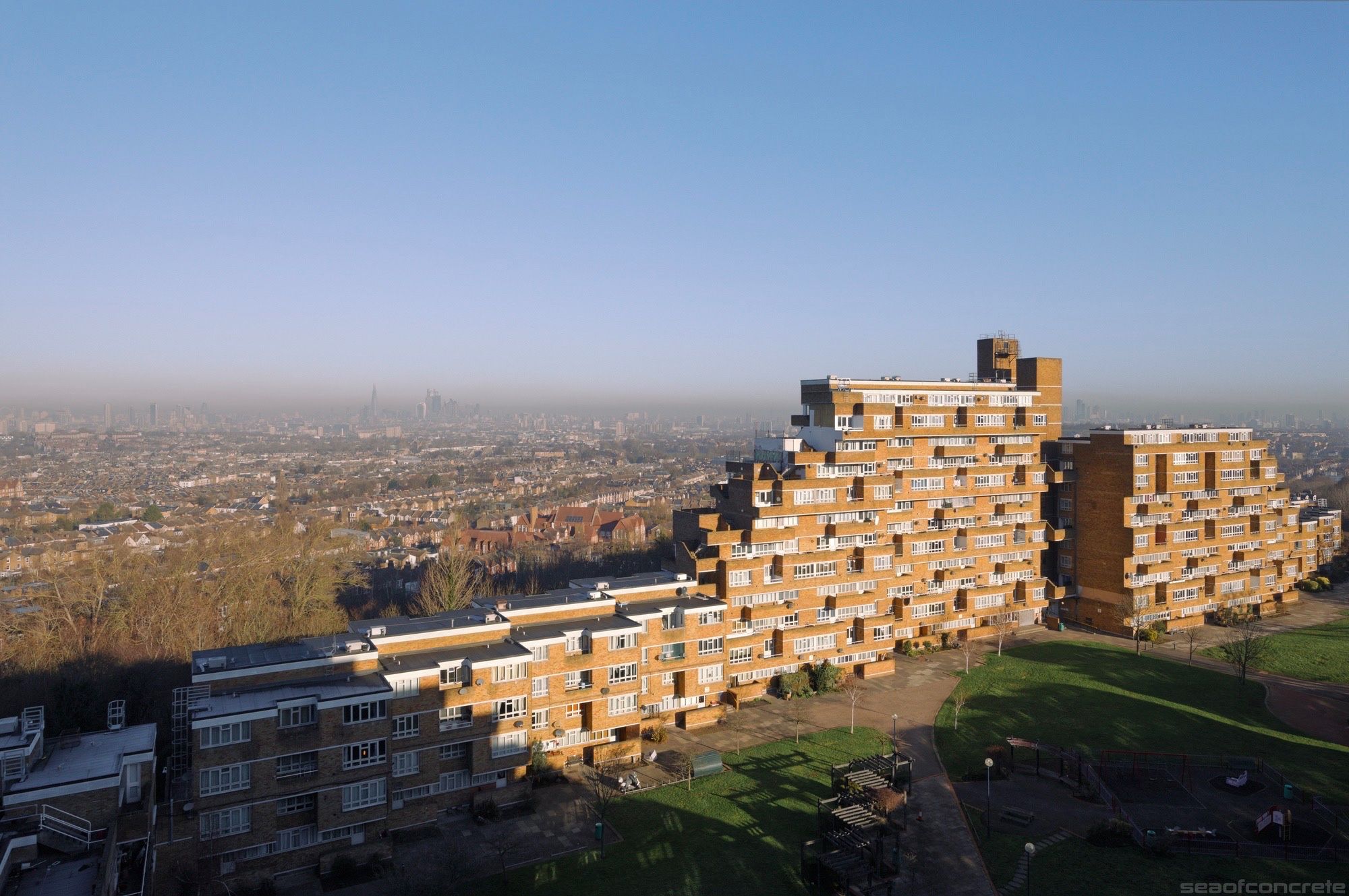 This photo is of the Ladlands block in the Dawson’s Heights estate, viewed from its twin, Bredinghurst block. The city of London is in the far distance, covered in a layer of thick smog. The skies are clear and the block is lit by the early morning sun.