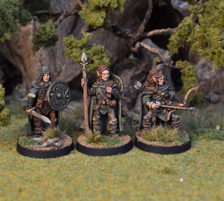 three model elves in drab greens and browns that blend into their forest surroundings. one carries a sword and shield, one a spear, and the third a loaded bow.