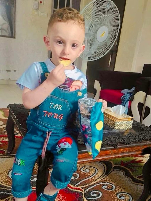 A photo of the martyr Sami Mahmoud , an adorable little boy sitting in a pair of overalls, eating a bag of chips