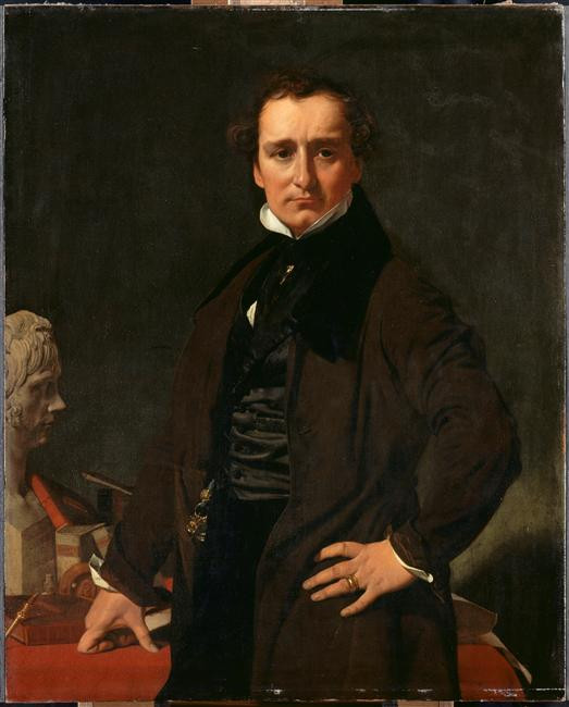 Portrait of the sculptor Lorenzo Bartolini by Ingres. Now in the Musée du Louvre, inv. RF 1942 24. https://collections.louvre.fr/en/ark:/53355/cl010066397
He is dressed as a gentleman in a black long coat, black vest, and trousers. His white shirt is visible at the color and a little under his black cravat. He proudly puts his left hand on his hip, as he stands in three-quarter view in front of a table where he has placed his right hand in an authoritative gesture with thumb and forefinger spread wide, the knuckle of his finger bent to lie on the table. The table holds a portrait bust, books, and instruments suggesting Bartolini's learning and artistic skill.