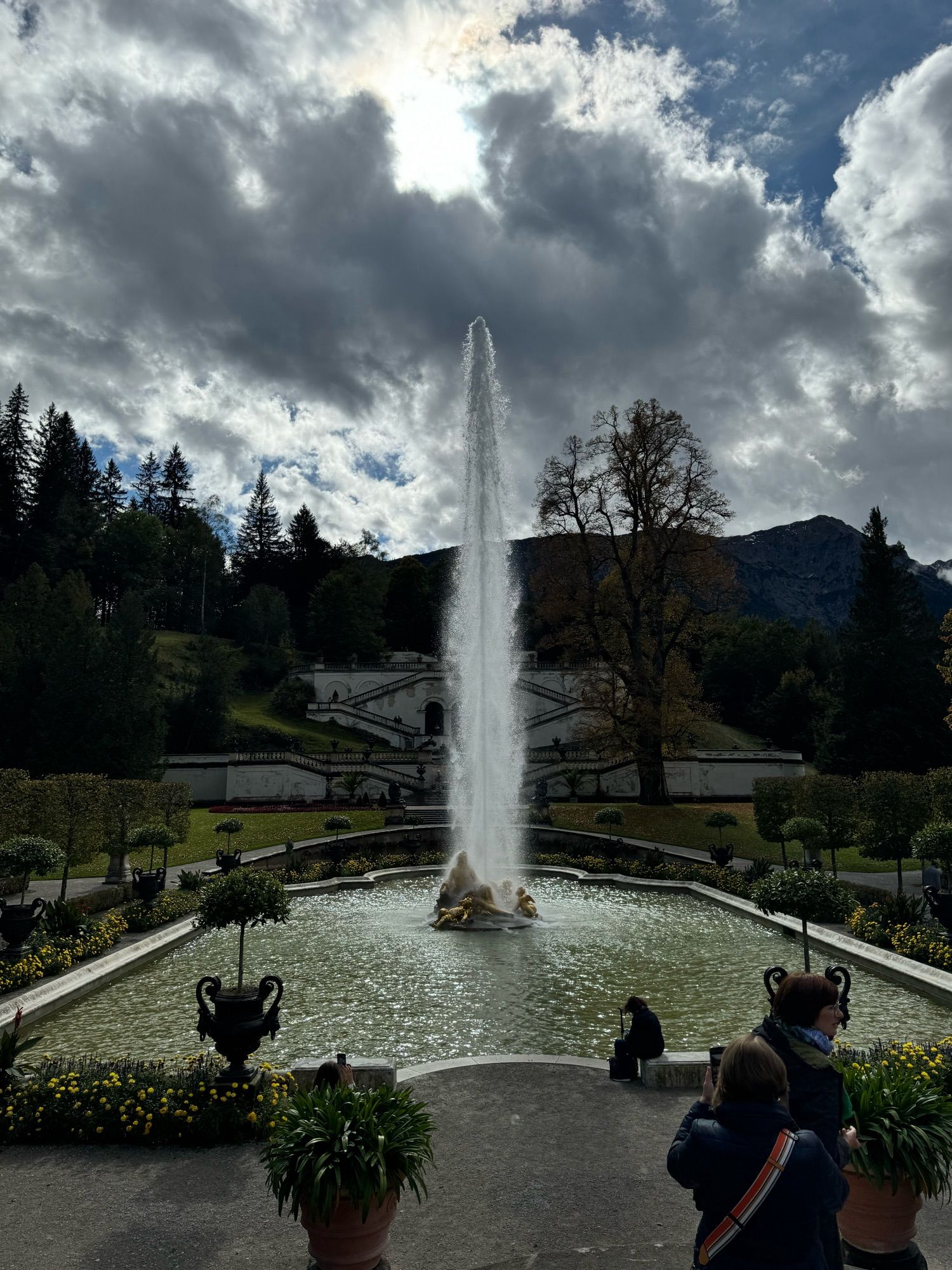 Fountain at Linderhof Palace. There are mountains in the background, clouds above lit by the sun.