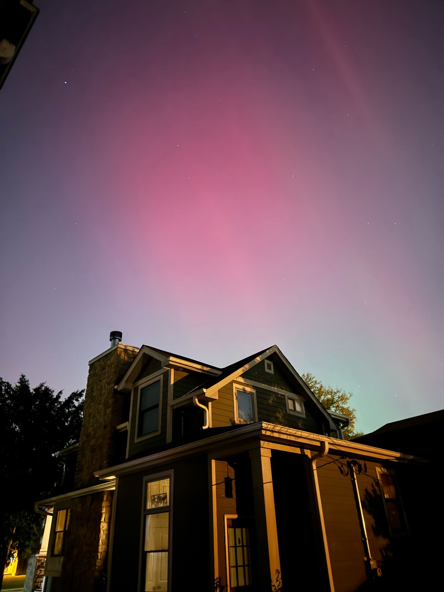 A pink and green Aurora shines above a house. 