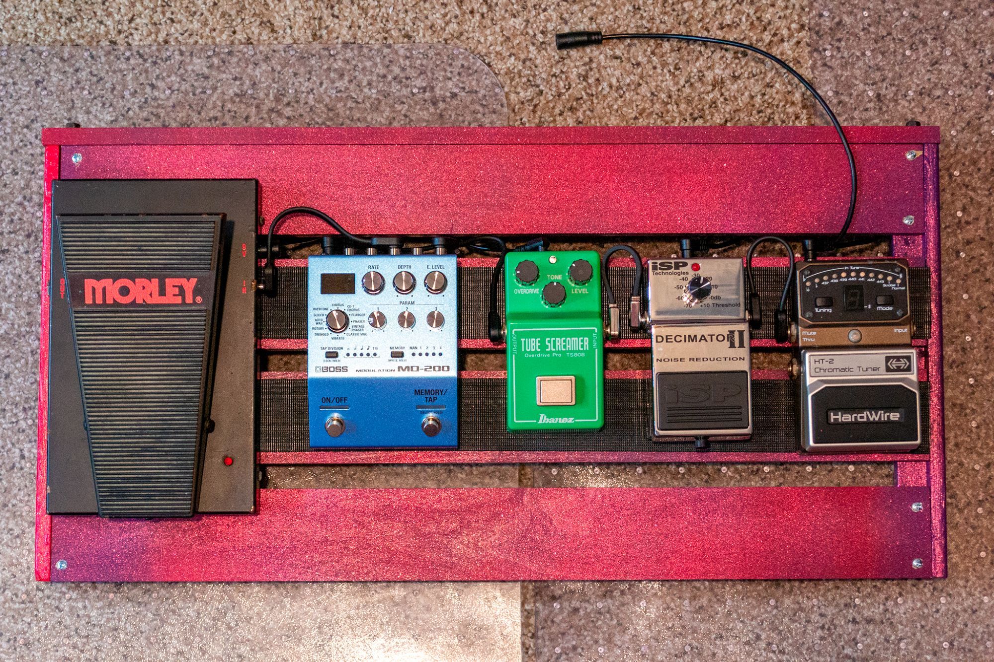 A bunch of guitar pedals are mounted on a red/magneta/purple pedalboard