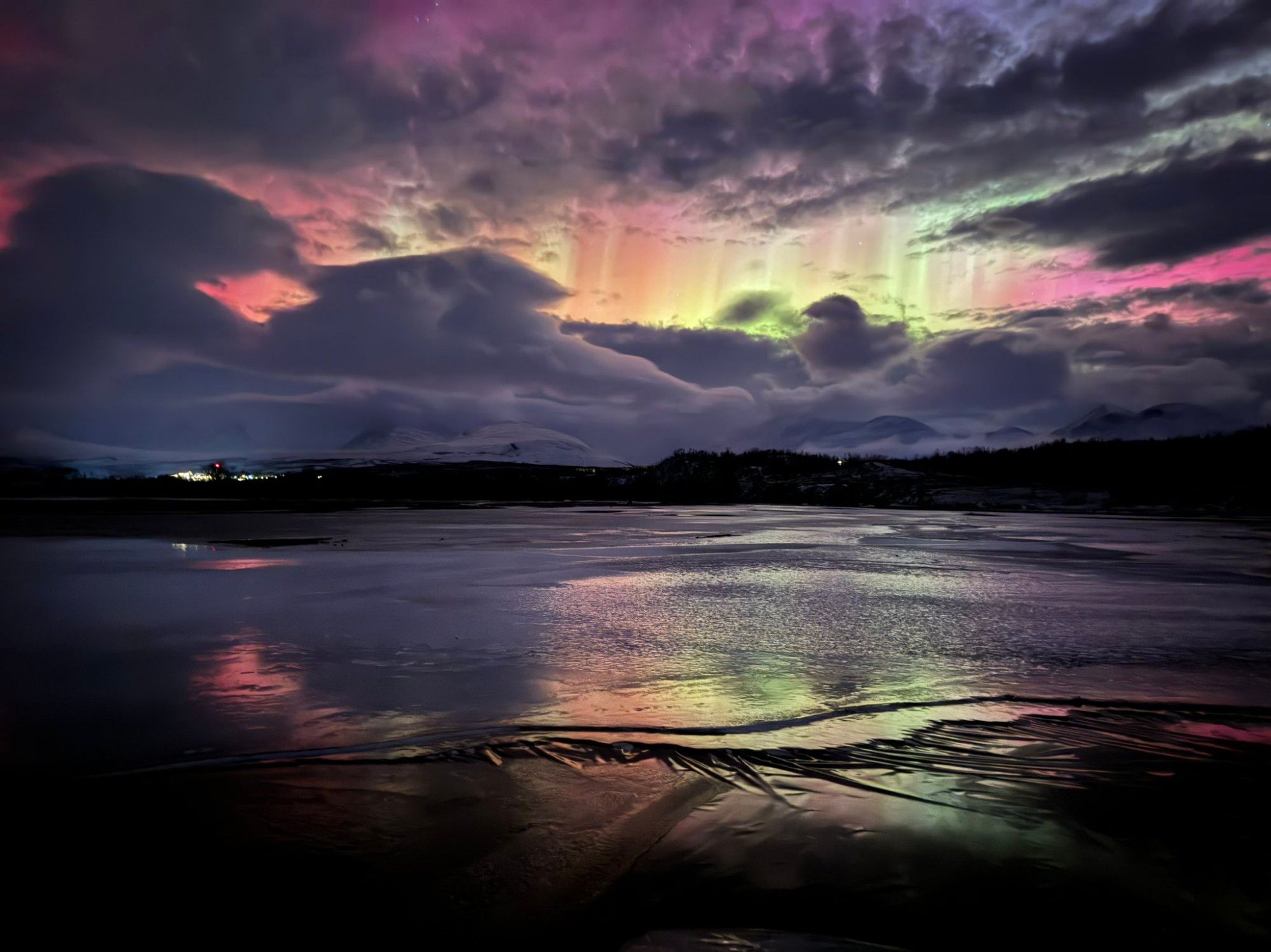 Au-dessus d'un lac gelé, un ciel nuageux arbore d'incroyables couleurs roses, orages, jaunes et vertes.