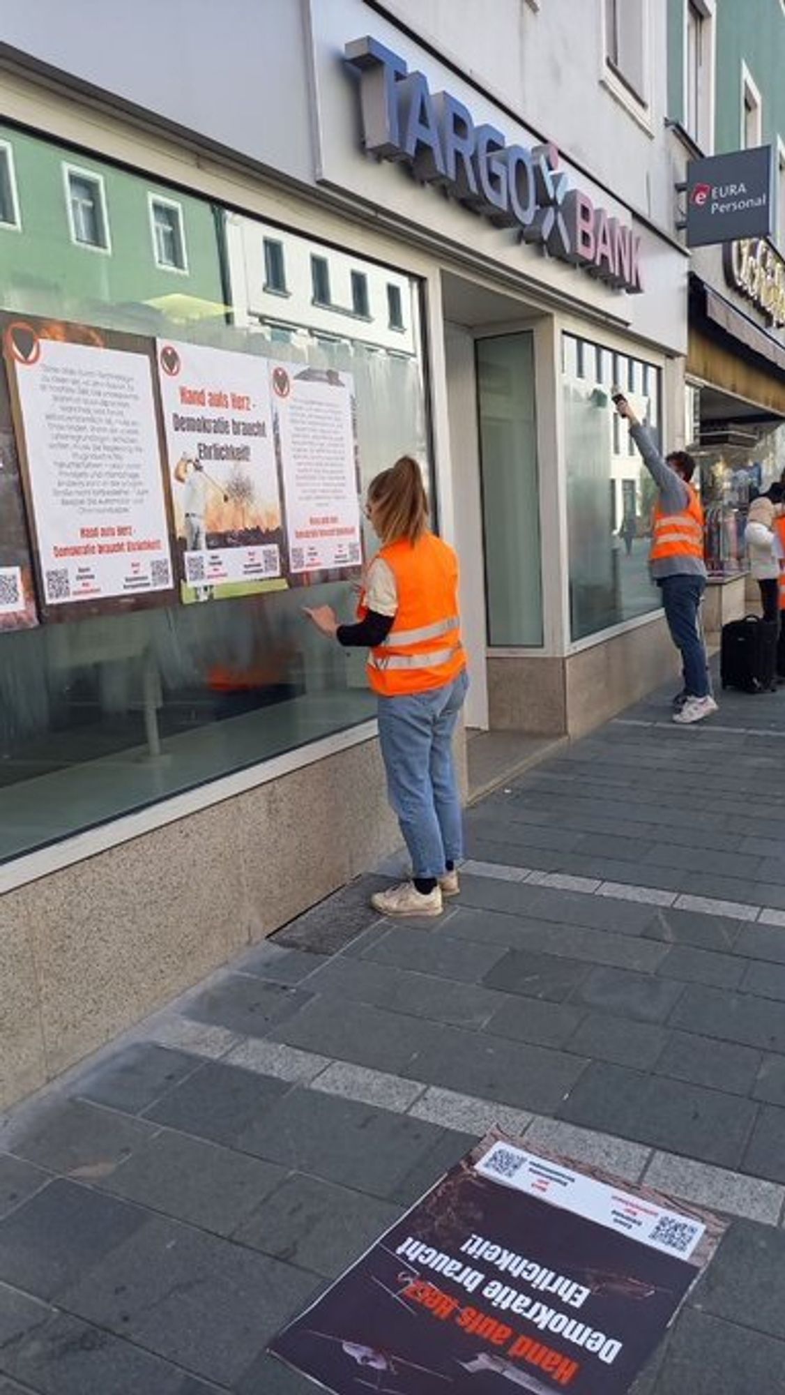 Menschen kleben Plakate an eine Targobank