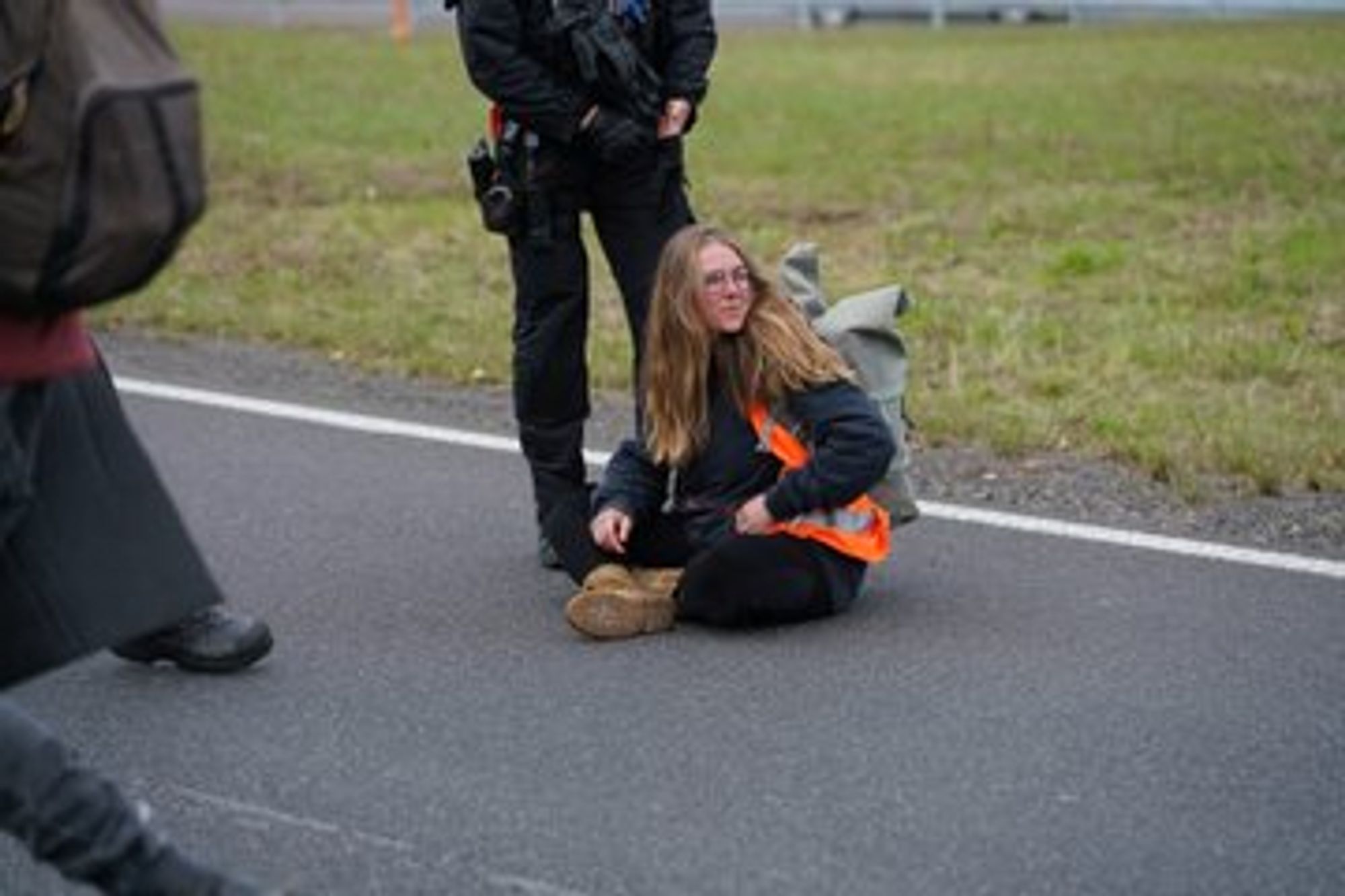 Eine Person in Warnweste sitze auf dem Boden vor einem Polizisten