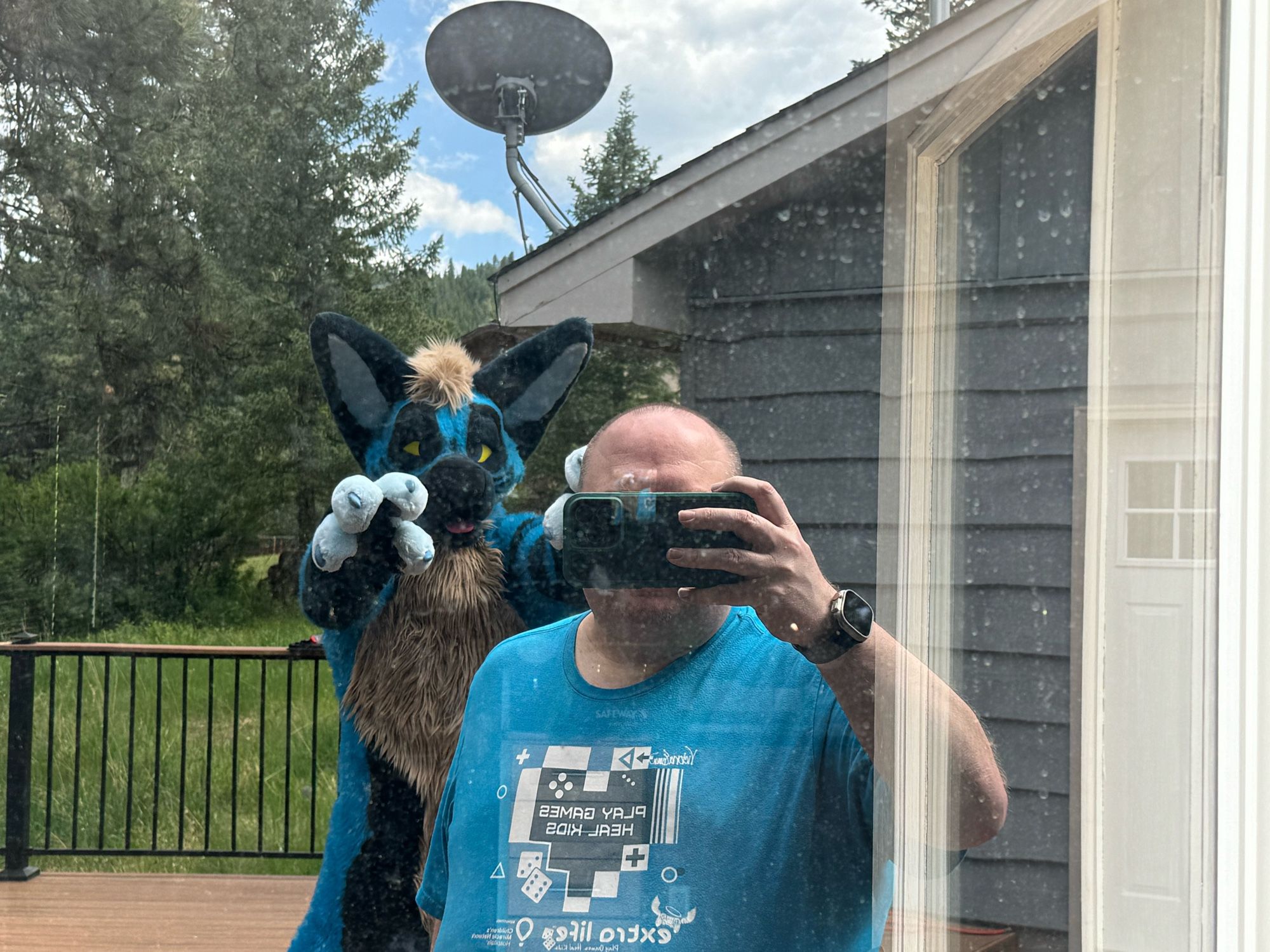 A photo of the reflection off a door shows me in a light blue Extra Life t-shirt with a blue hyena making grabby paws behind me.