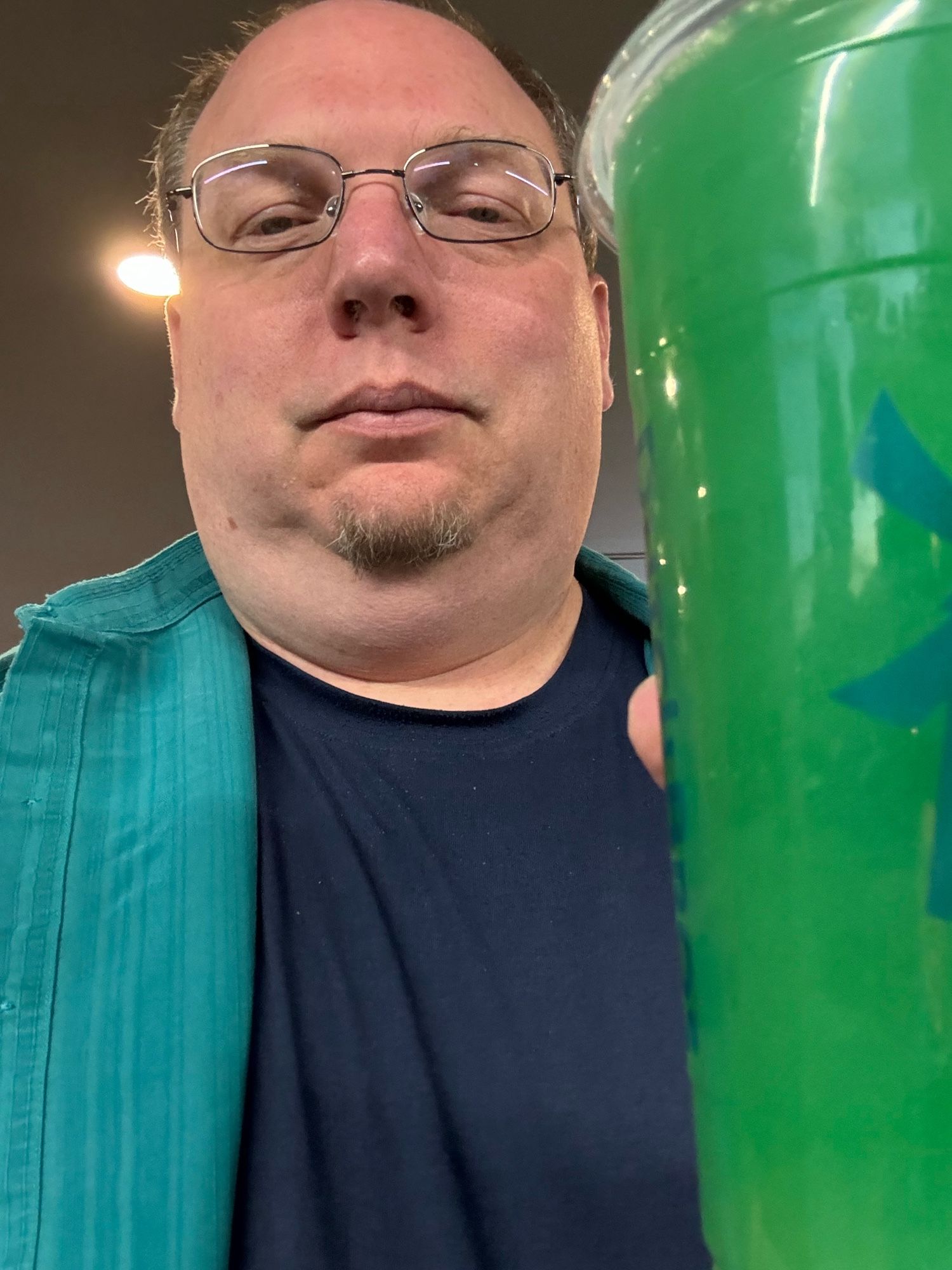 Me in a dark blue shirt and off-teal overshirt holding a bright green energy drink slush.